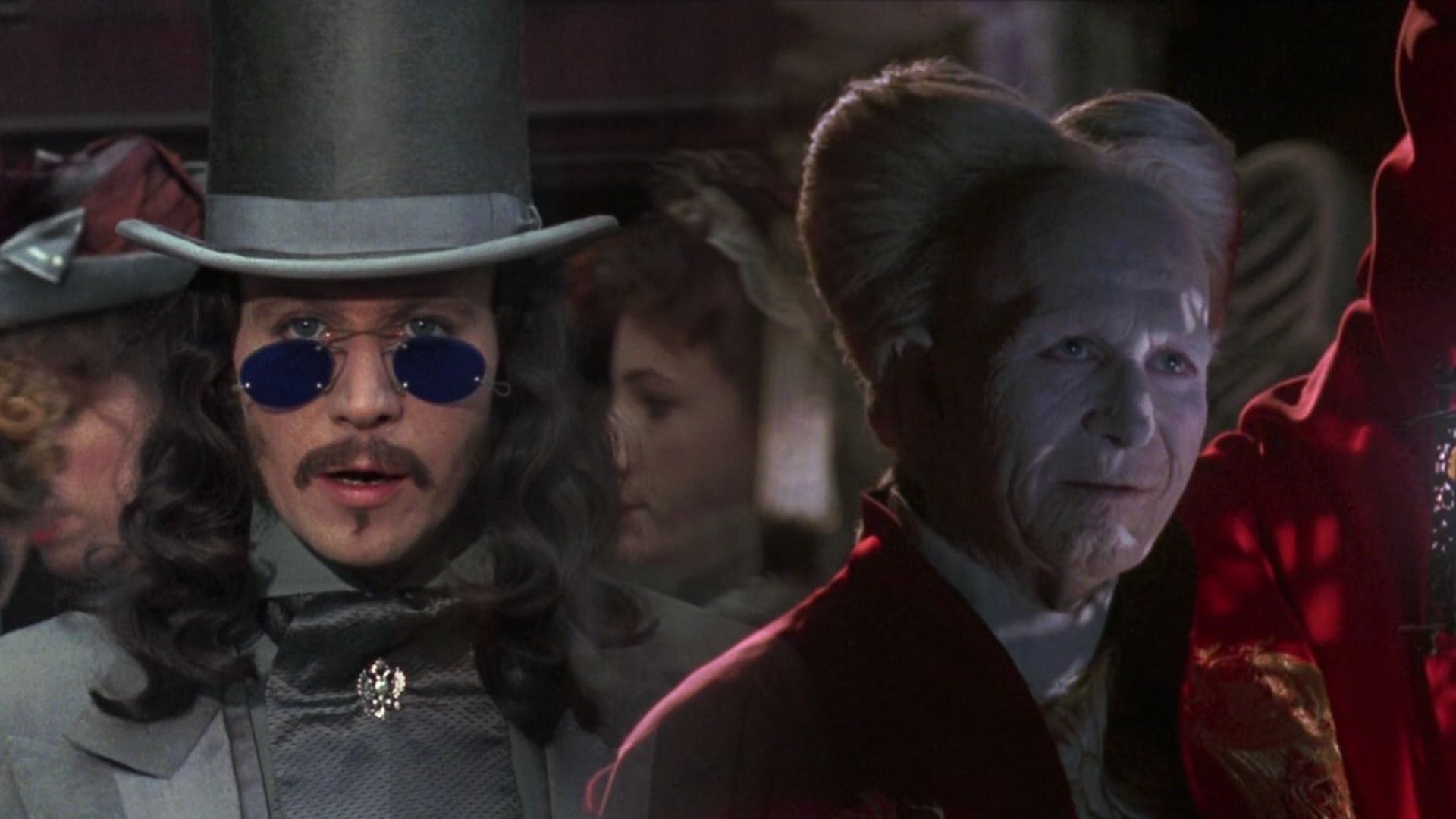 Aktor Gary Oldman w szarym garniturze i kapeluszu, po prawej w czerwonej szacie z białymi włosami