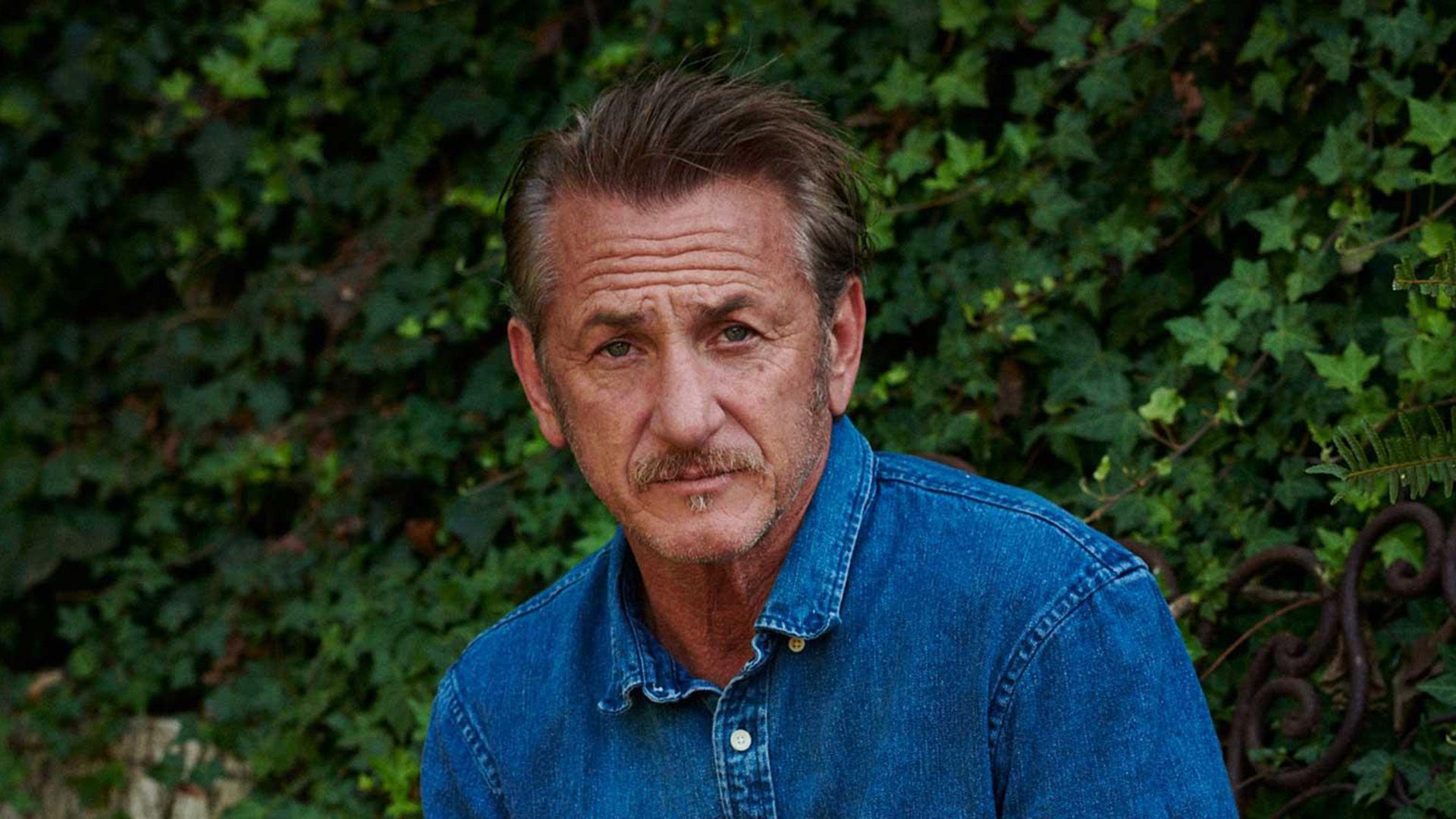 Sean Penn w dżinsowej koszuli na tle zielonego bluszczu