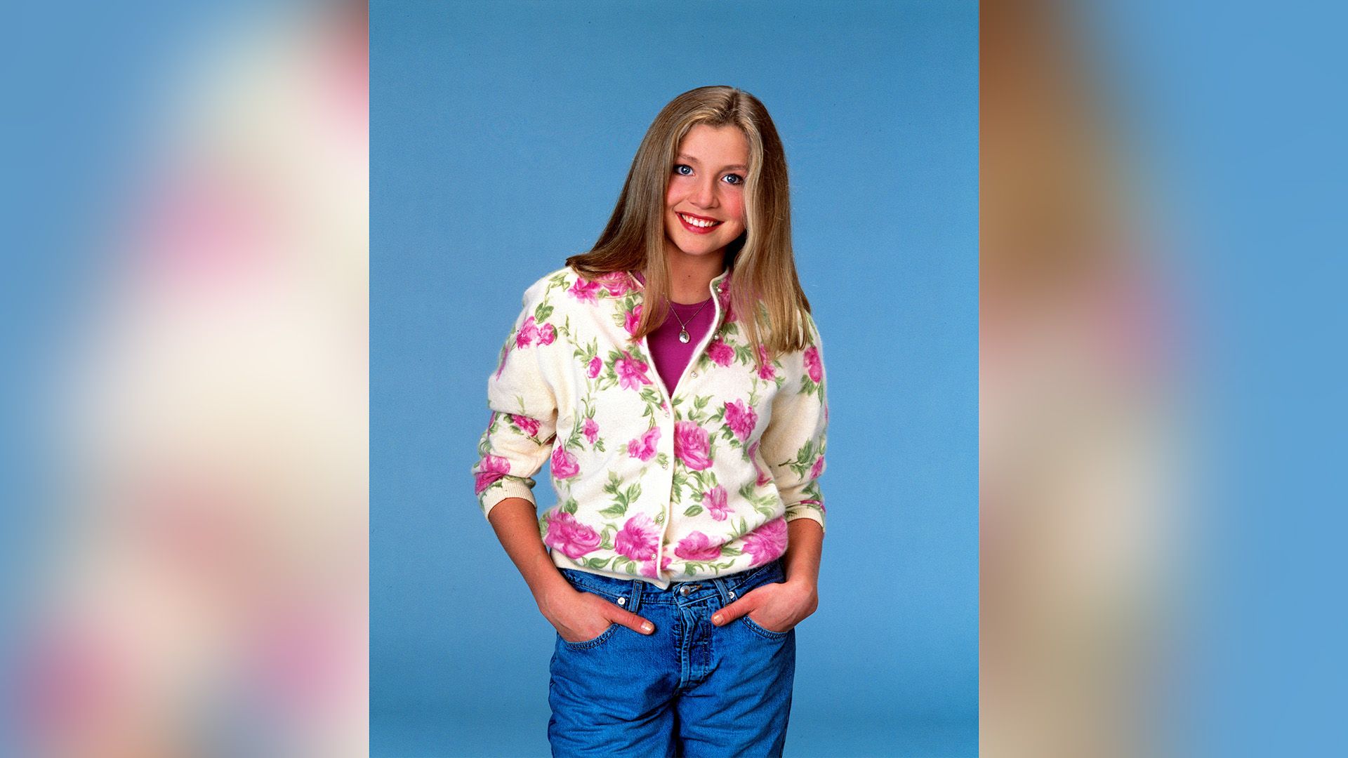 Sarah Chalke w dżinsach i białym swetrze z dużymi różowymi kwiatami