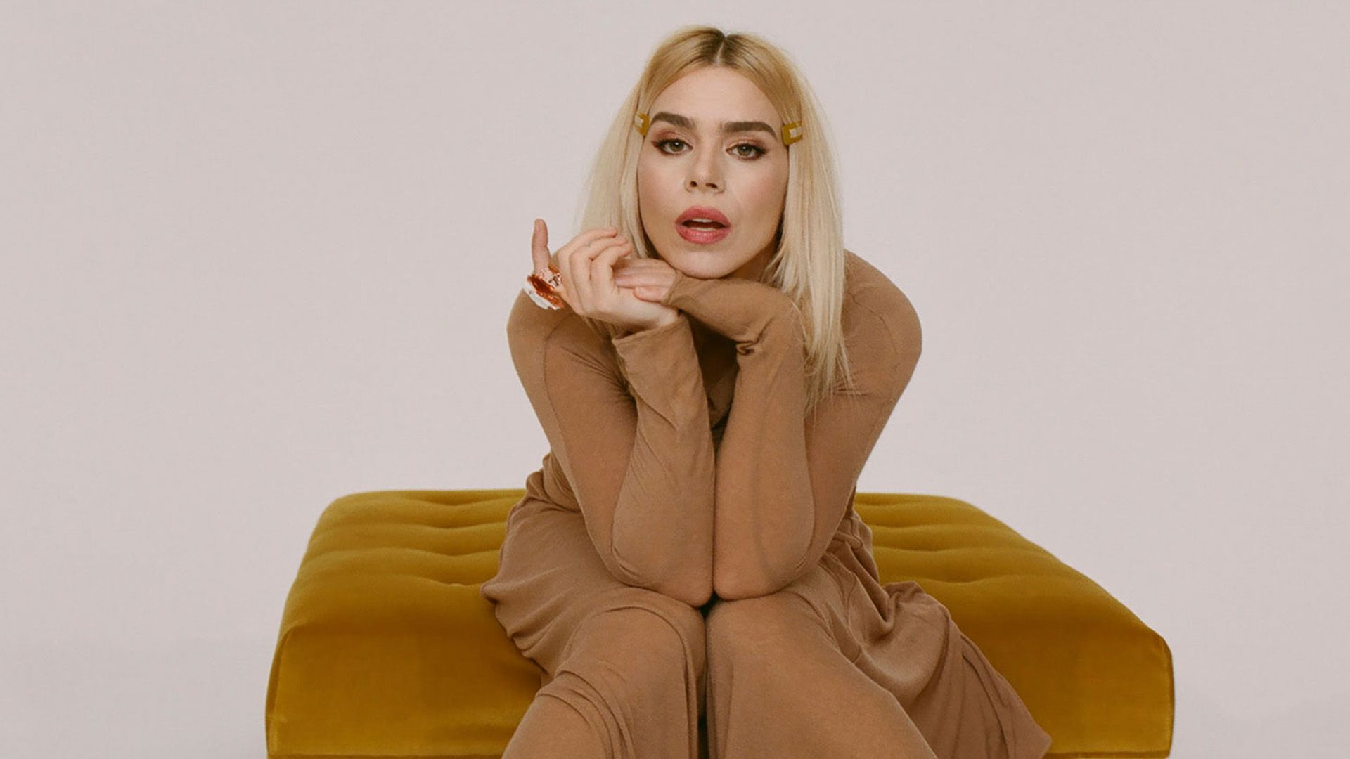 Billie Piper w długiej beżowej sukni siedzi w rudym fotelu