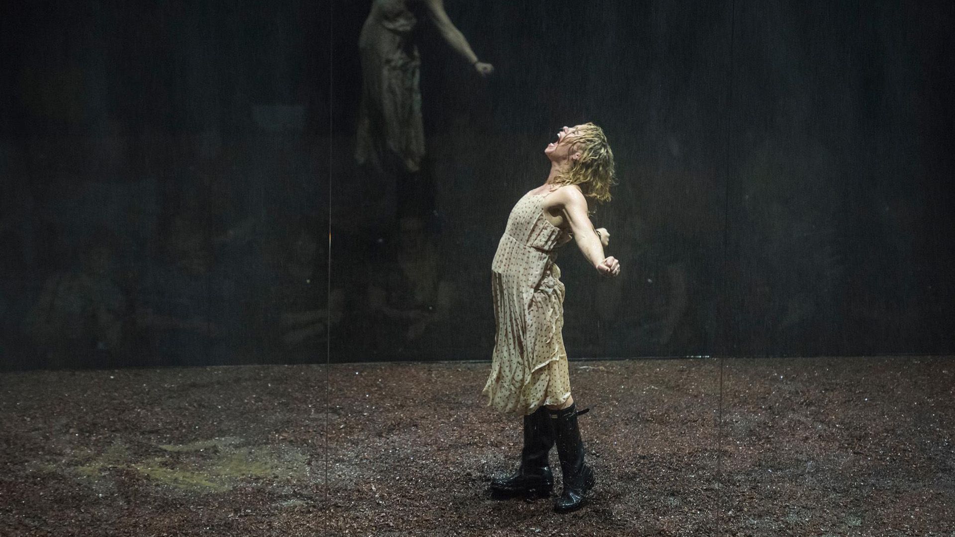 Billie Piper w jasnej sukience i wysokich butach stoi na scenie z rozłożonymi ramionami, krzycząc