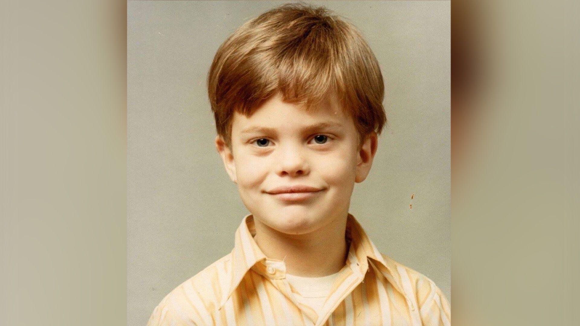 Rainn Wilson jako dziecko w pasiastej koszulce na beżowym tle