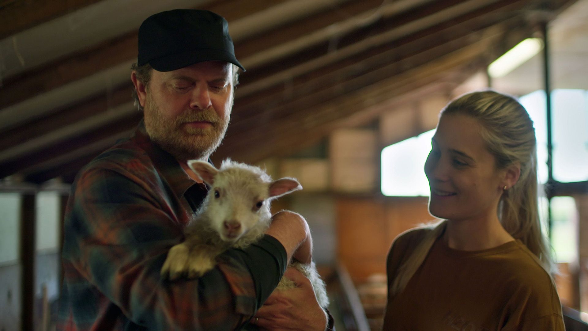 Rainn Wilson trzymający koźlątko z uśmiechniętą dziewczyną stojącą obok niego