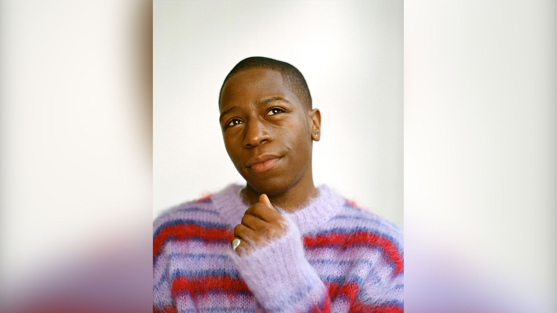 David Jonsson w puszystym czerwono-fioletowym swetrze w paski patrzy marzycielsko w górę