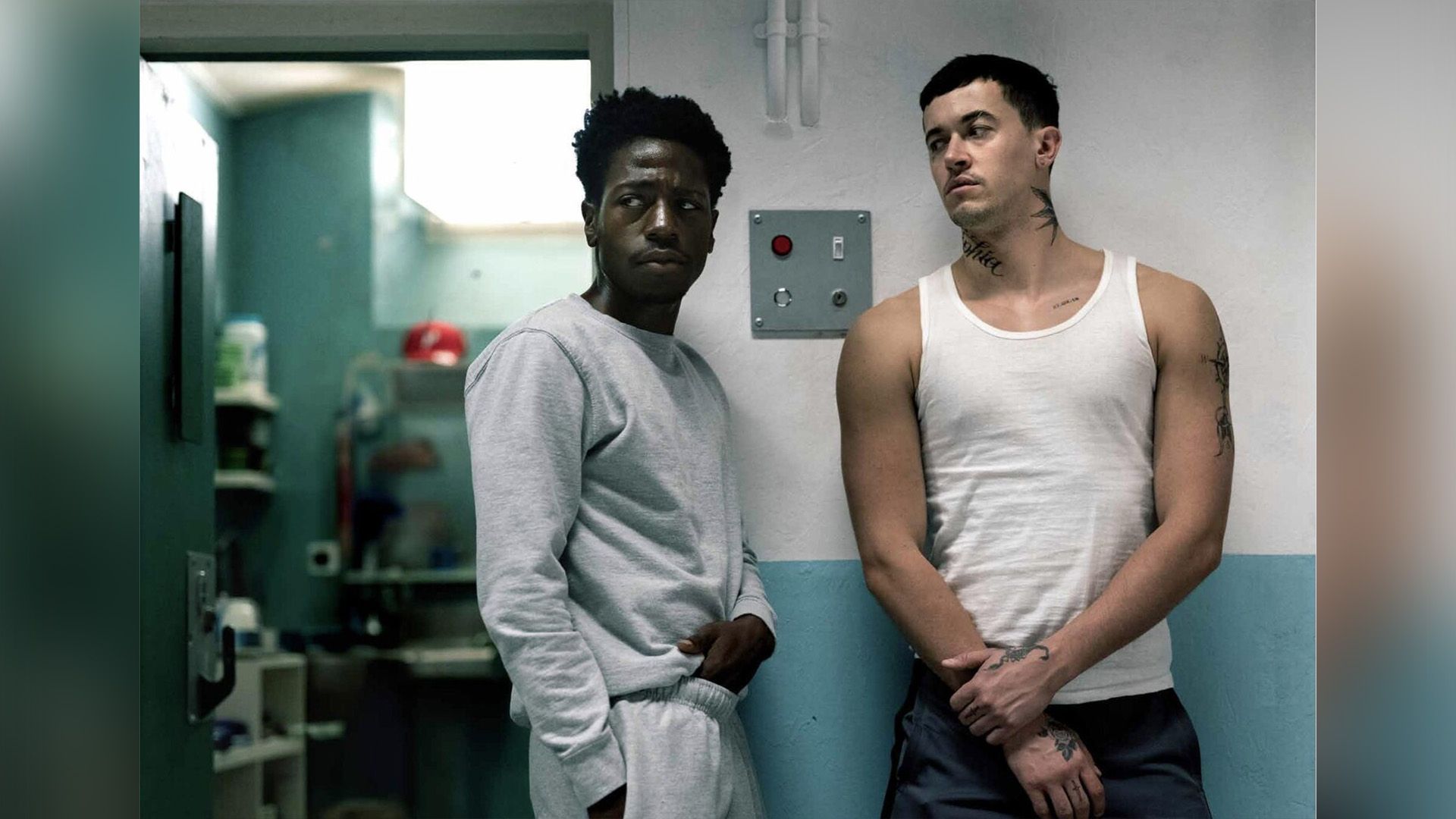 David Jonsson w szarym dresie stoi przy celi więziennej obok wysokiego mężczyzny w białym podkoszulku