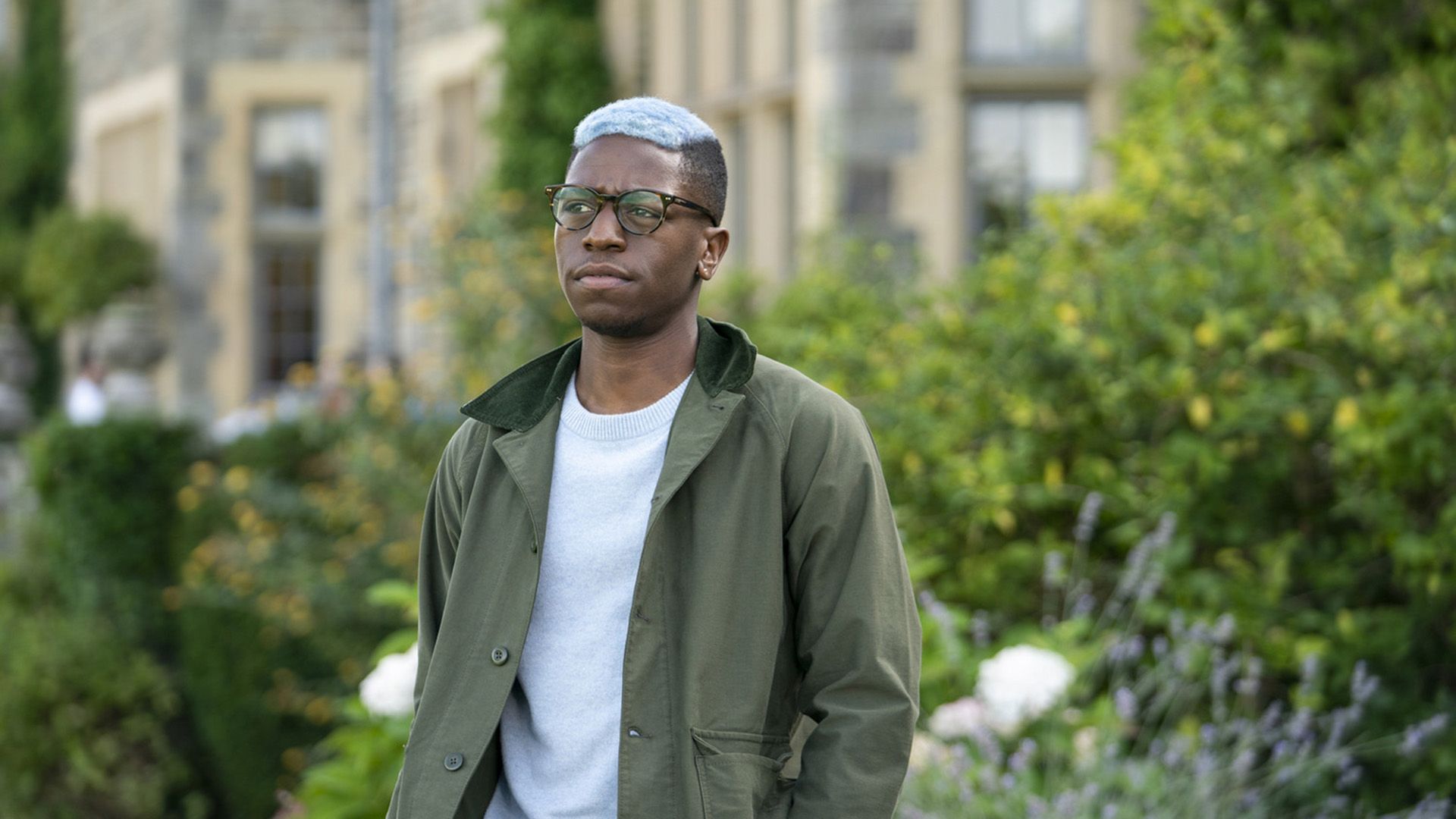 David Jonsson w okularach i z niebieskimi włosami stoi na ulicy w zielonej kurtce