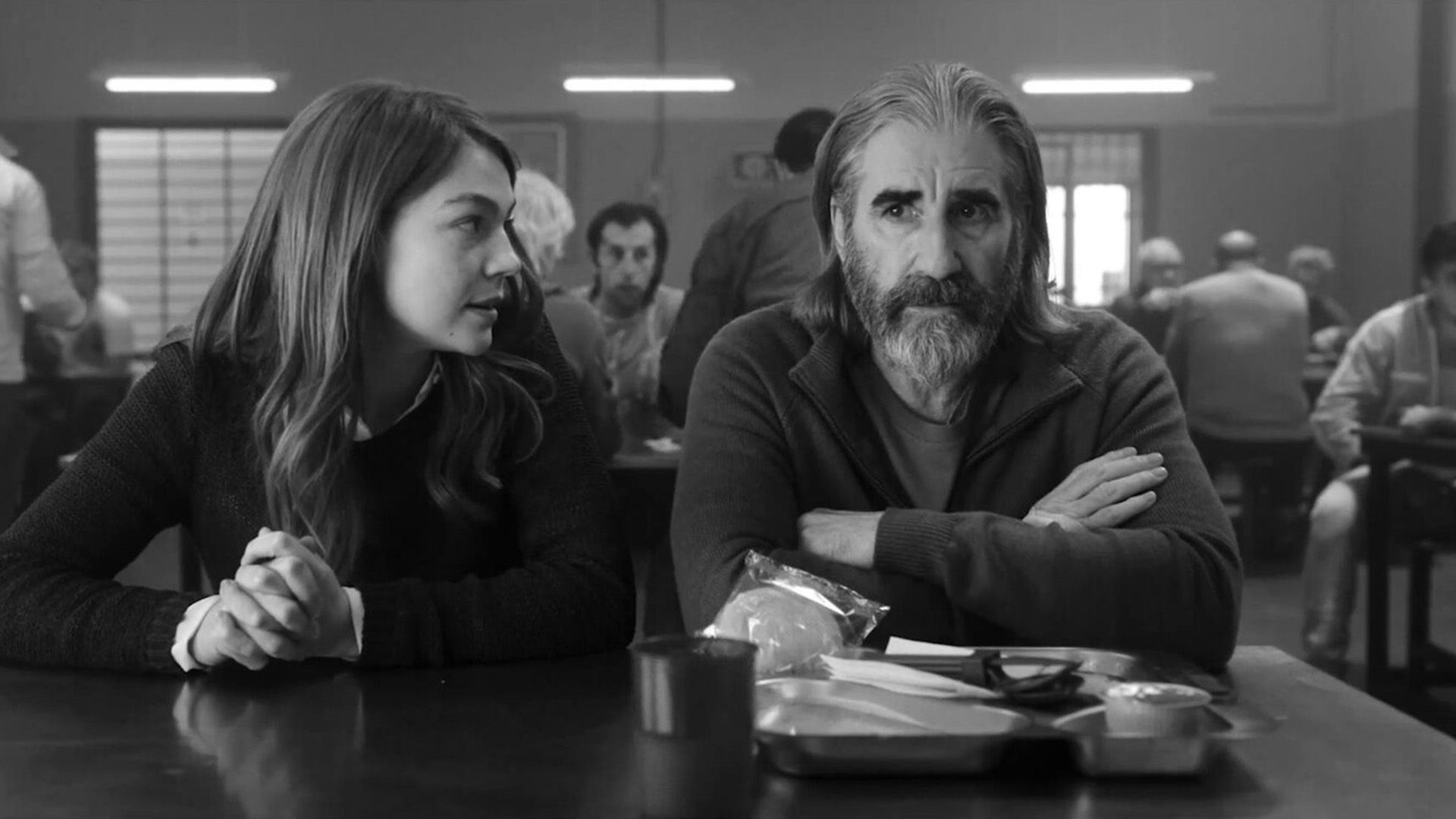 John Lynch siedzi przy stole w stołówce, obok niego siedzi dziewczyna, która coś mówi