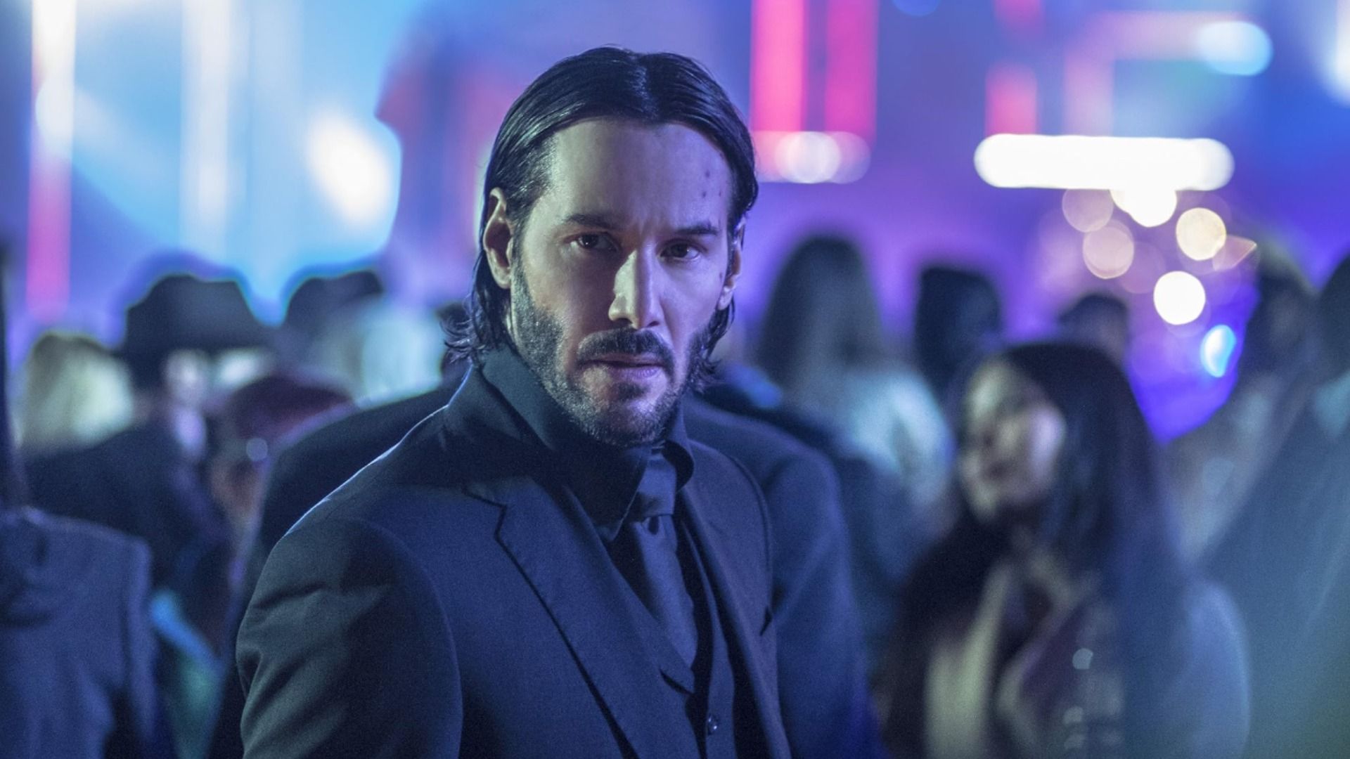 Aktor Keanu Reeves z długimi włosami w czarnym klasycznym garniturze