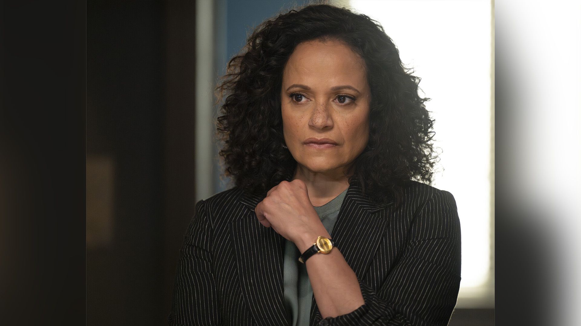 Judy Reyes w pasiastej marynarce patrzy zamyślona w bok