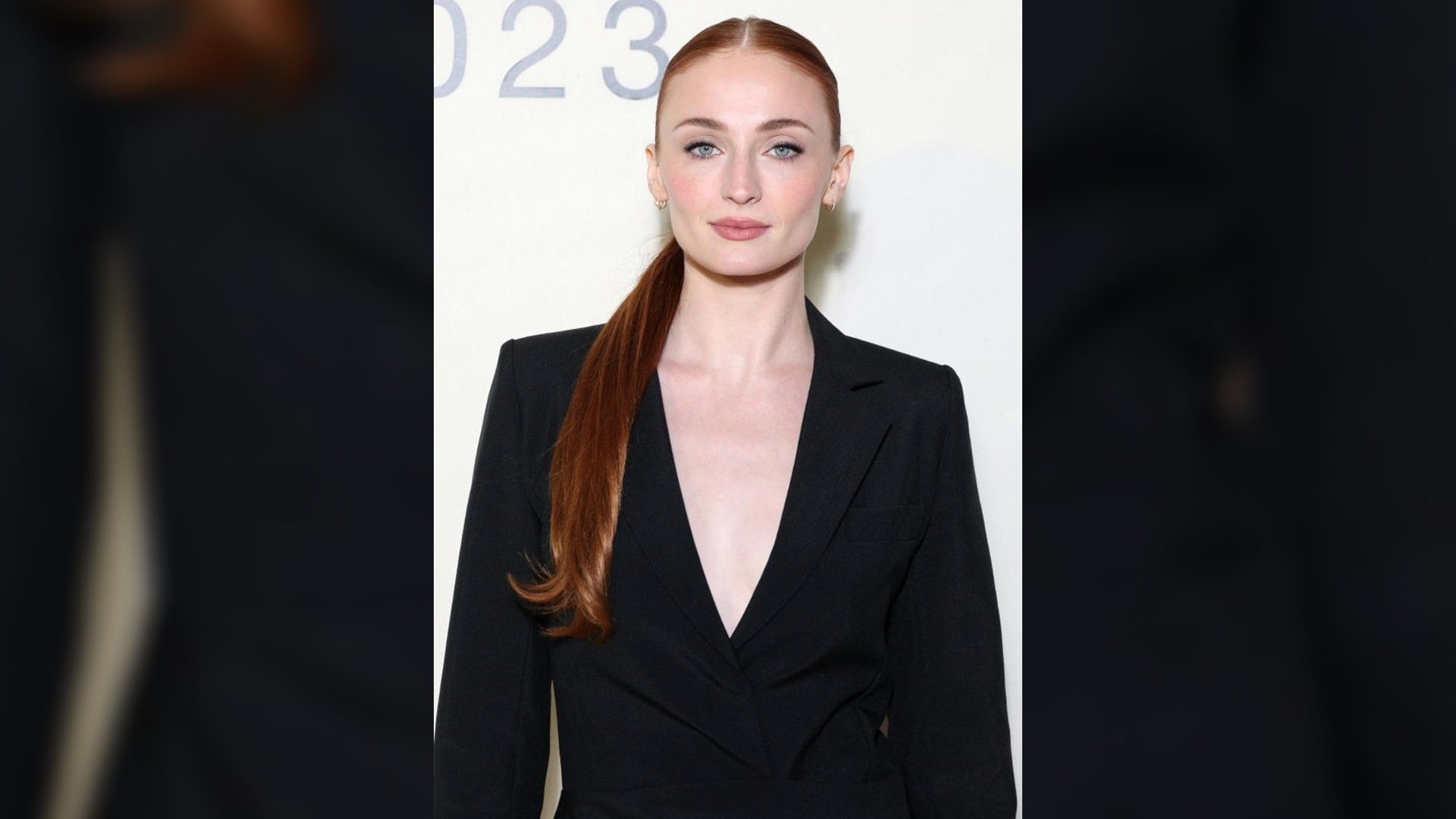 Aktorka Sophie Turner fotografowana od pasa w górę. Włosy w kucyku i marynarka