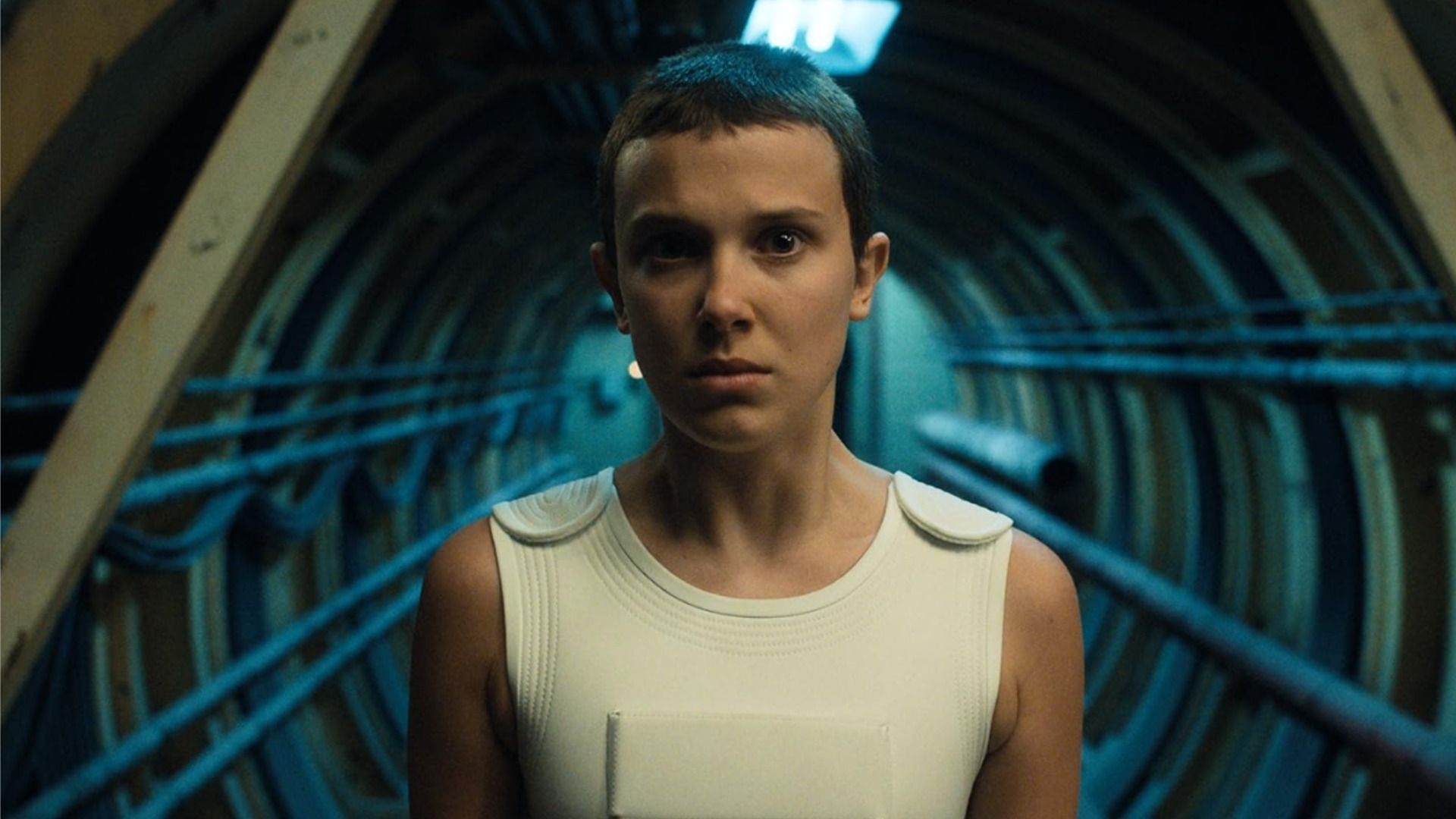 Millie Bobby Brown z krótką fryzurą stoi w tunelu i patrzy w kamerę