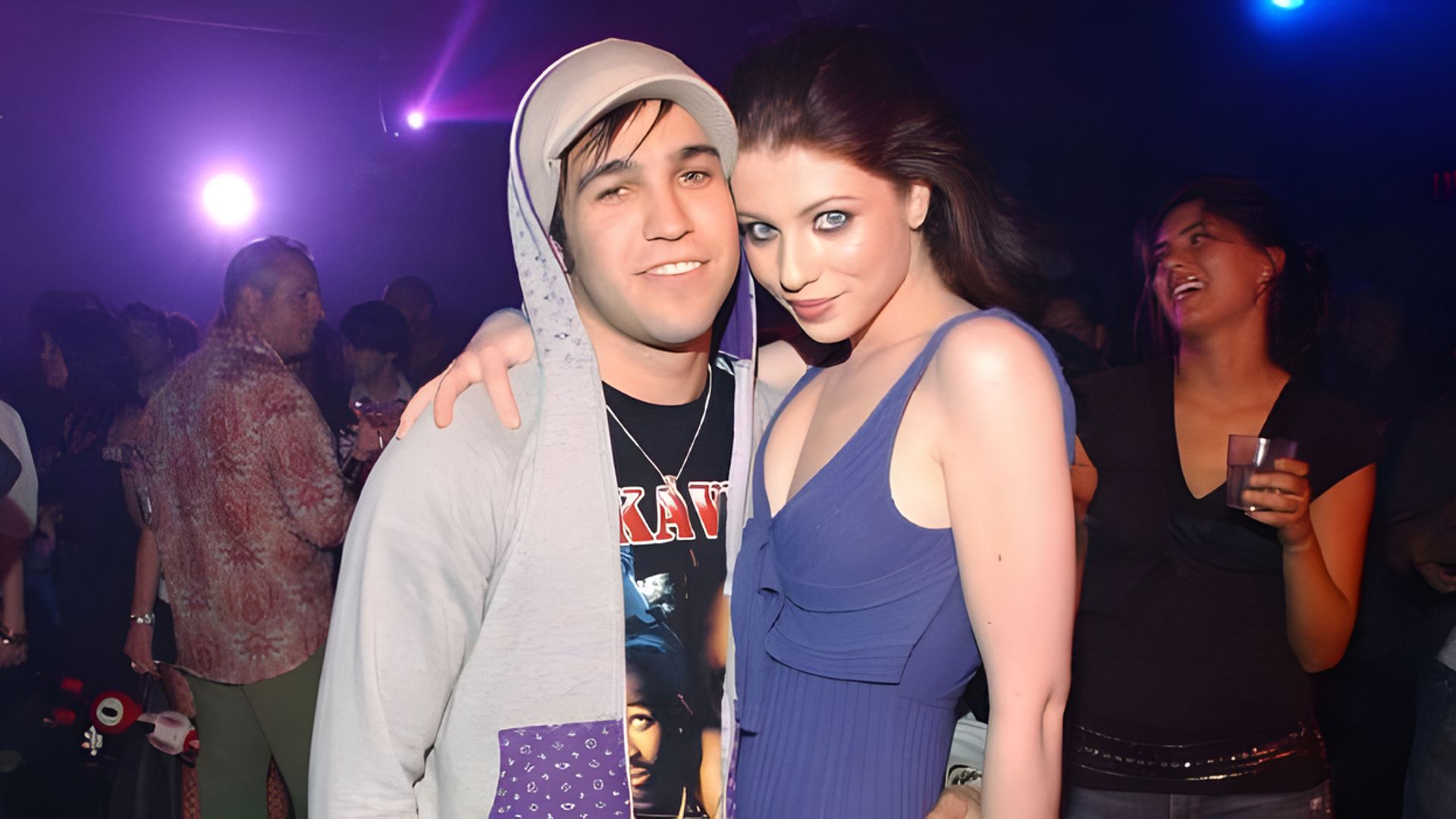 Aktorka Michelle Trachtenberg i muzyk Pete Wentz przytulają się, podczas gdy w tle ludzie się bawią