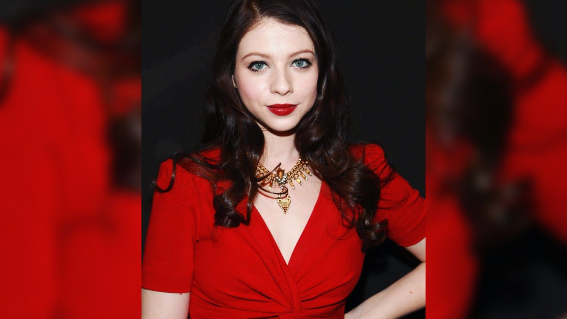 Aktorka Michelle Trachtenberg w czerwonej sukience i jaskrawym makijażu z czerwonymi ustami pasującymi do koloru sukienki