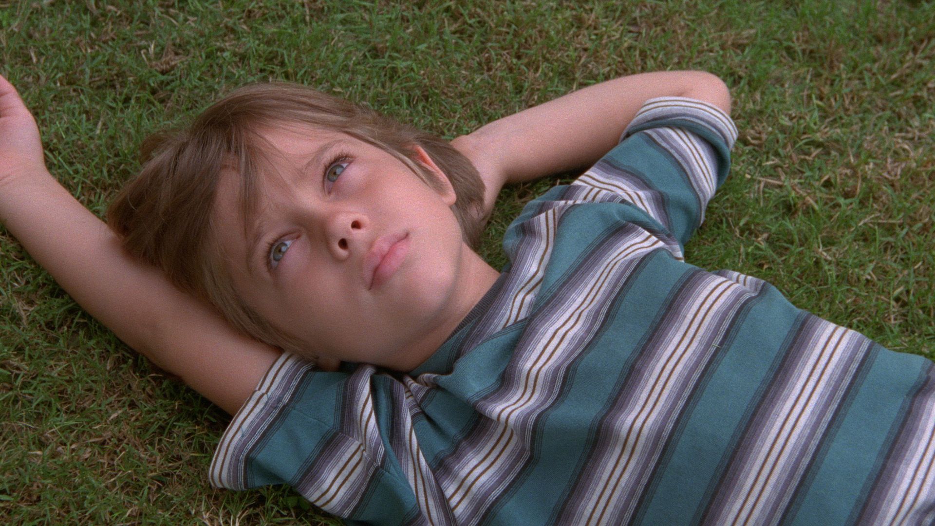 Kadr z filmu "Boyhood": młody Ellar Coltrane w koszulce w paski leży na trawie