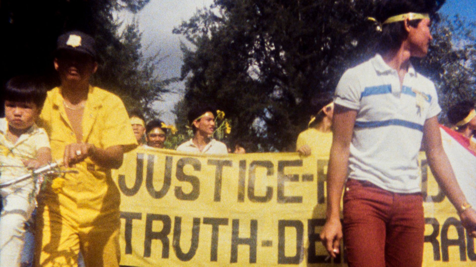 Kadr z filmu "Why is Yellow the Middle of the Rainbow?": grupa ludzi z żółtym plakatem na demonstracji