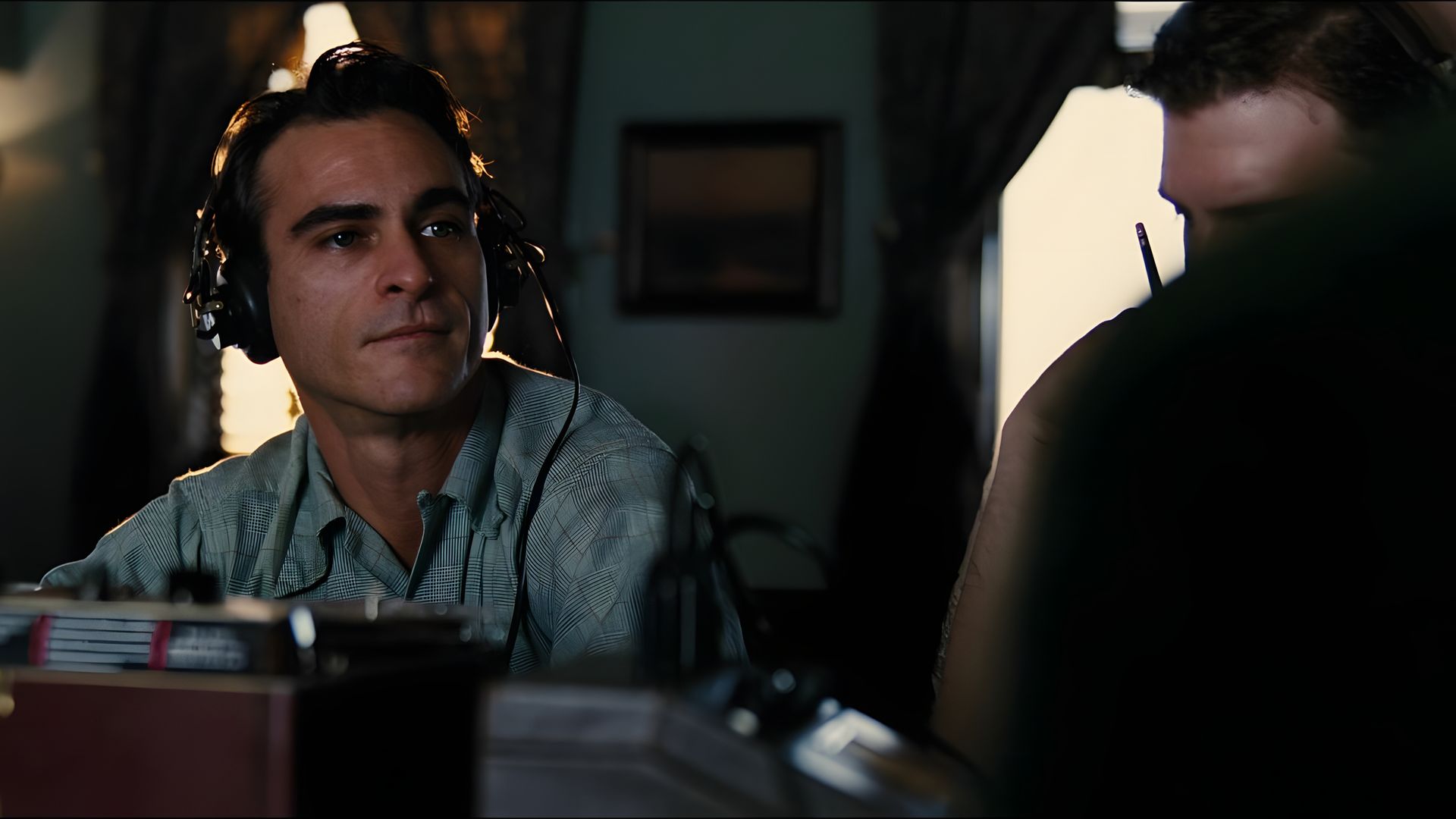 Joaquin Phoenix w niebieskiej koszuli i dużych słuchawkach patrzy w dal