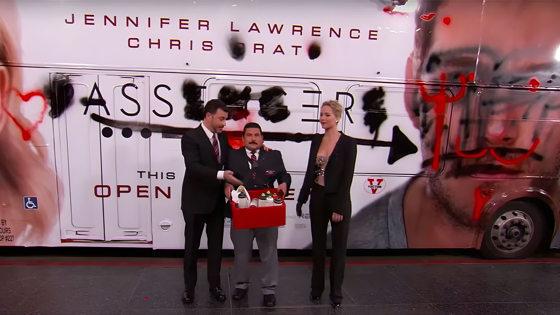 Jimmy Kimmel z asystentem i Jennifer Lawrence stoją przy autobusie pokrytym graffiti