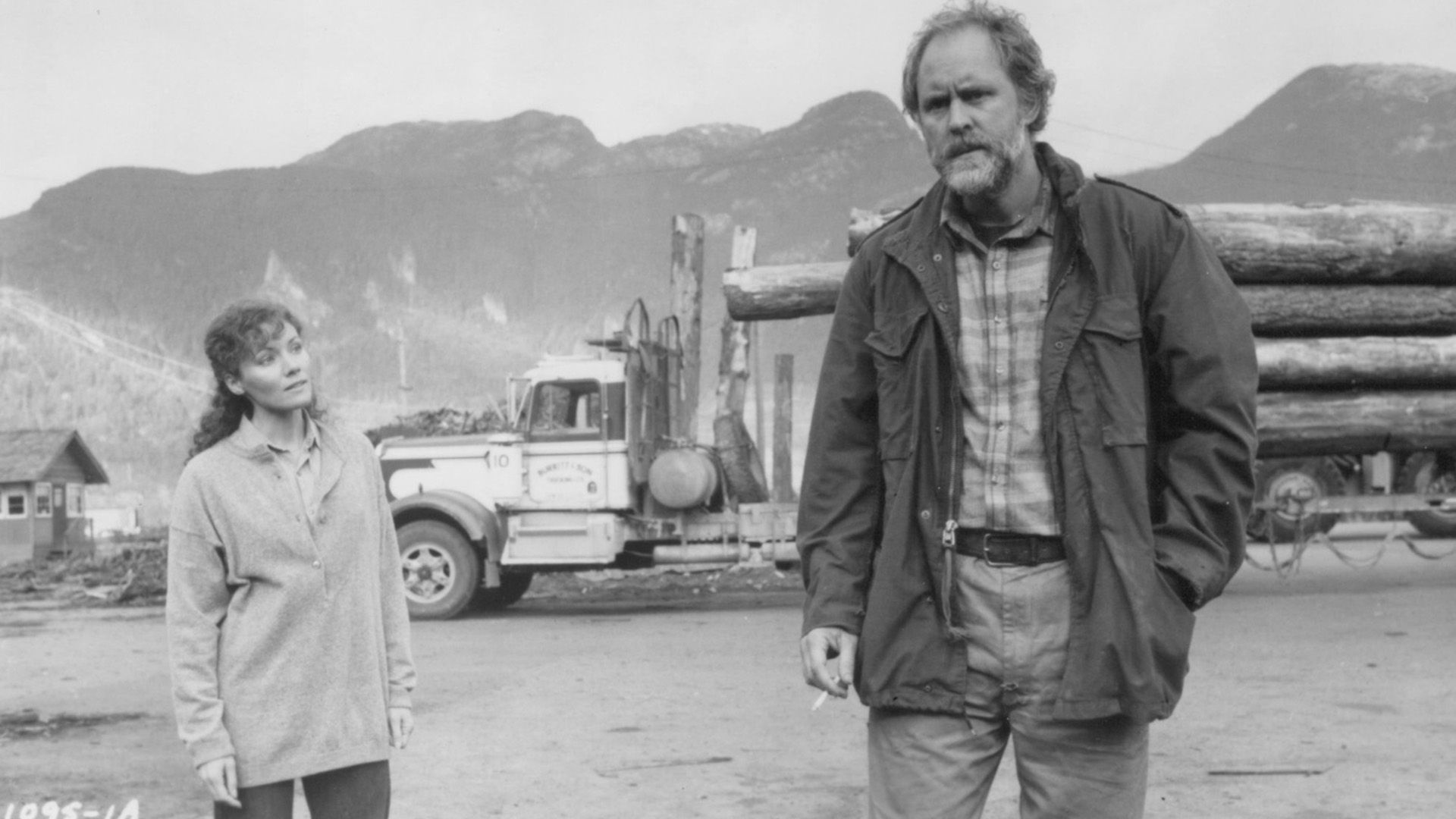 John Lithgow w podartych ubraniach stoi na tle ciężarówki do przewozu drewna w scenie z filmu "Distant Thunder"