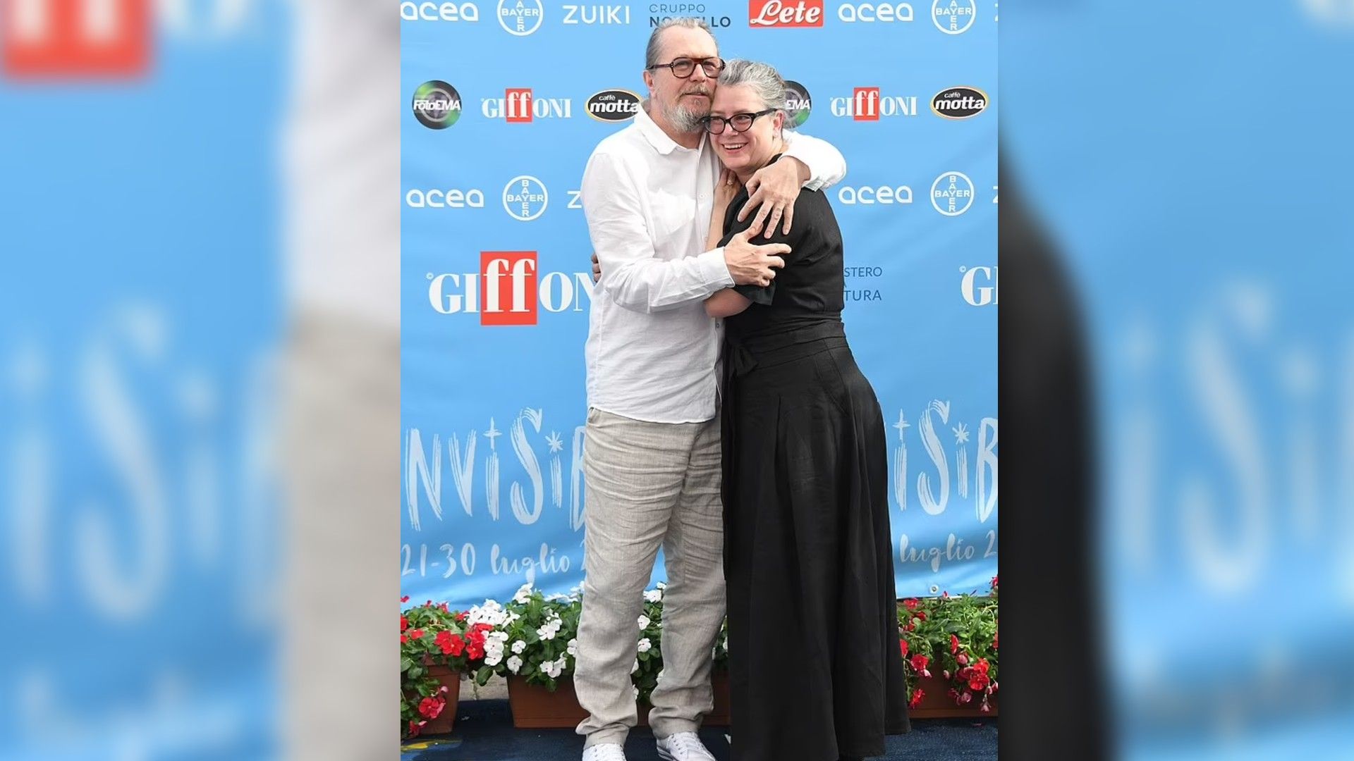Gary Oldman i Gisele Schmidt przytulają się i uśmiechają na tle niebieskiego bannera z logo Giffoni