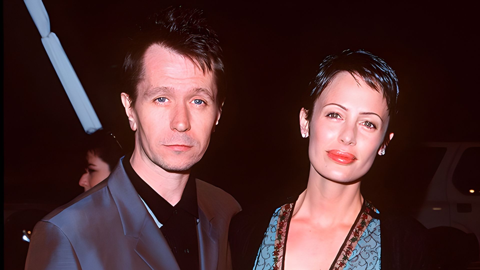 Gary Oldman w ciemnym garniturze i Donya Fiorentino w eleganckiej sukni pozują razem na wieczornym wydarzeniu.