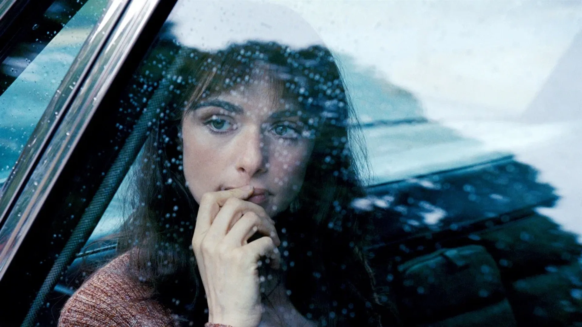 Zbliżenie na twarz aktorki Rachel Weisz sfotografowanej przez szybę samochodu w deszczu