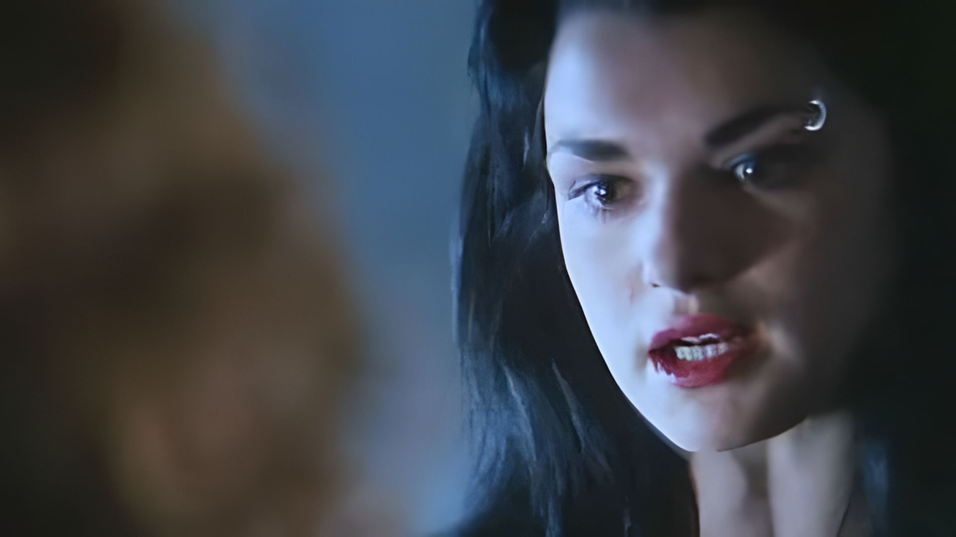 Zbliżenie na twarz Rachel Weisz, ma jaskrawoczerwone usta i kolczyk w brwi