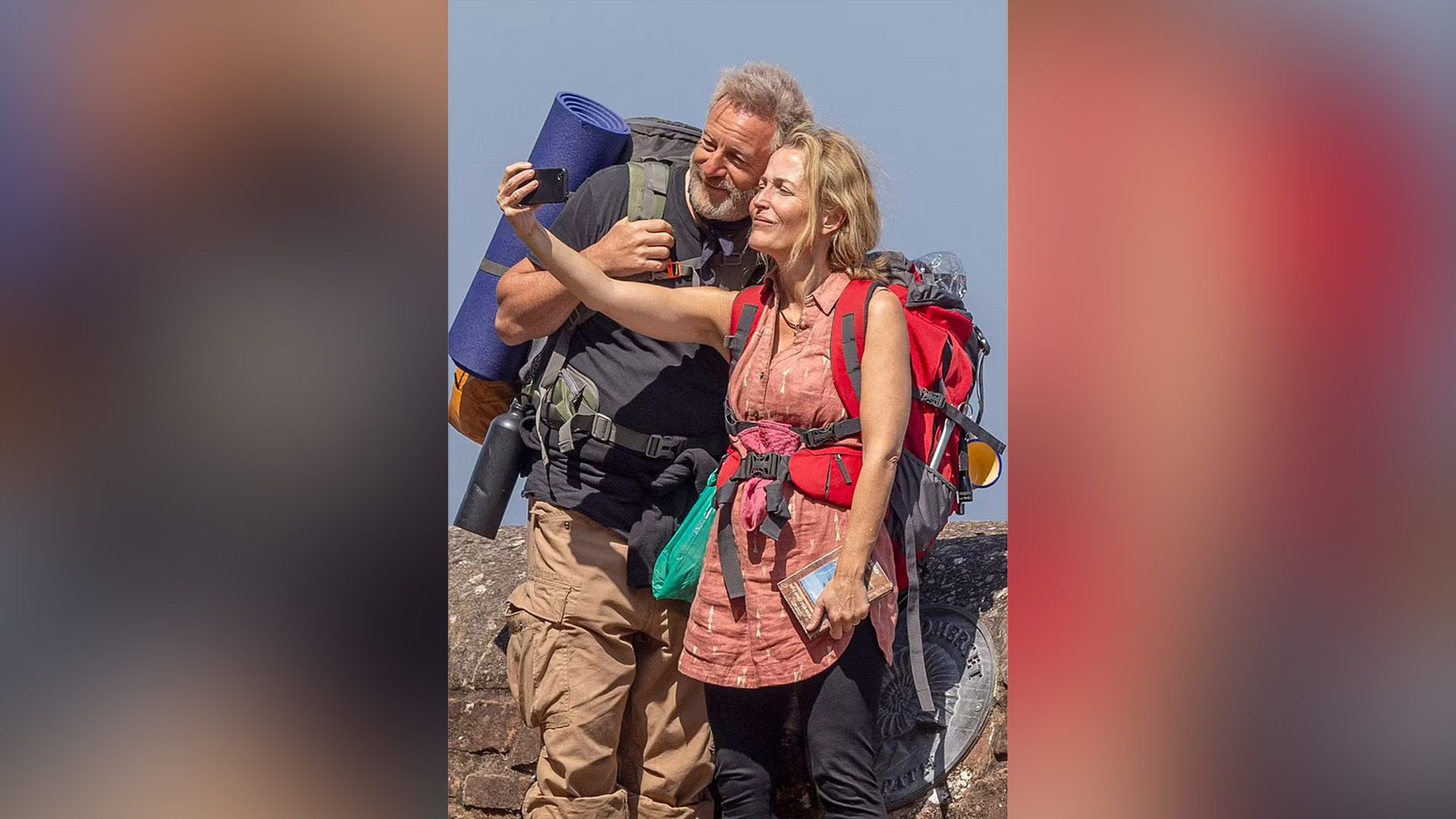 Jason Isaacs i Gillian Anderson z plecakami na plecach robią selfie telefonem