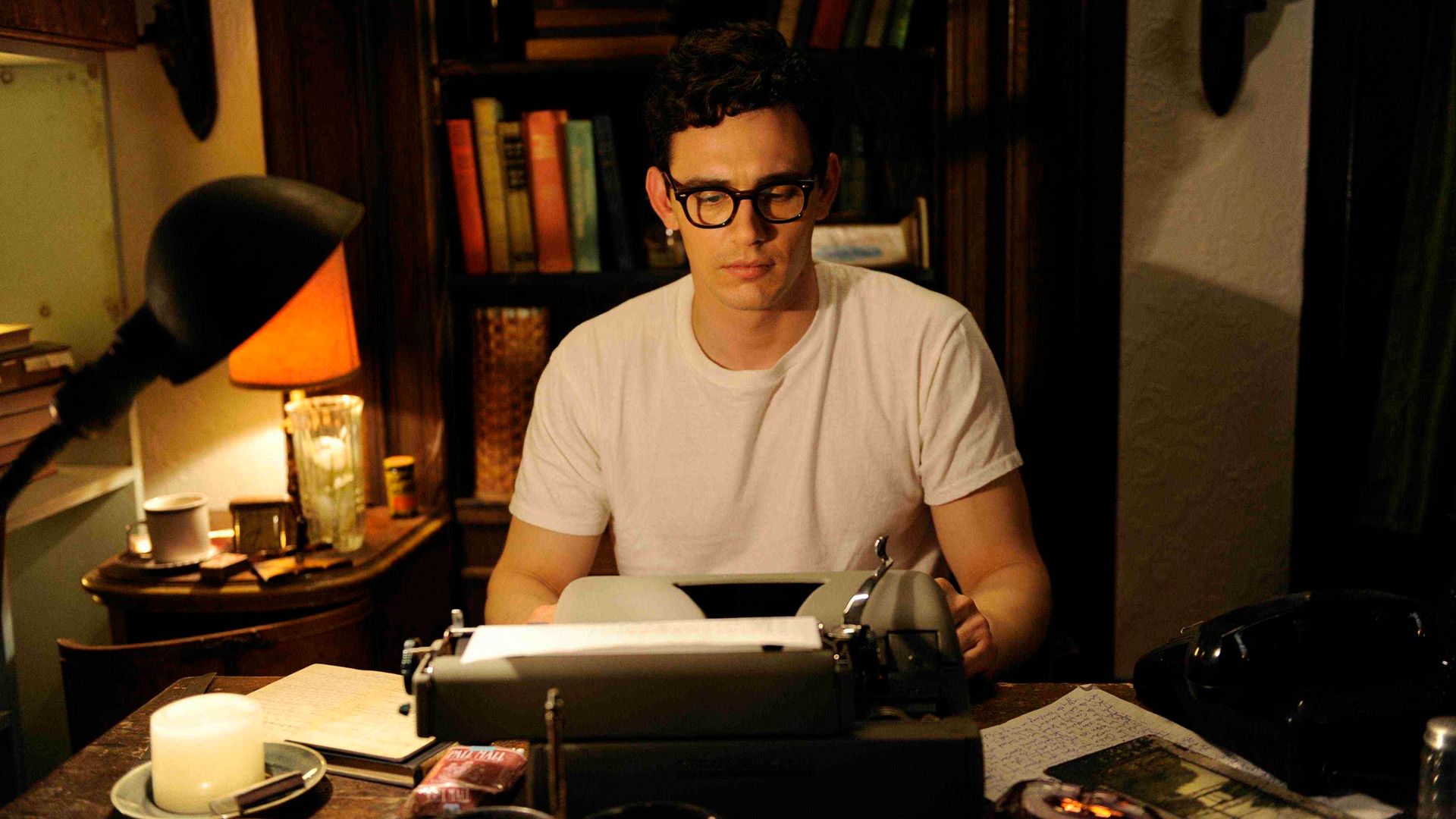 James Franco, ubrany w białą koszulkę i okulary w czarnej oprawce, przy maszynie do pisania