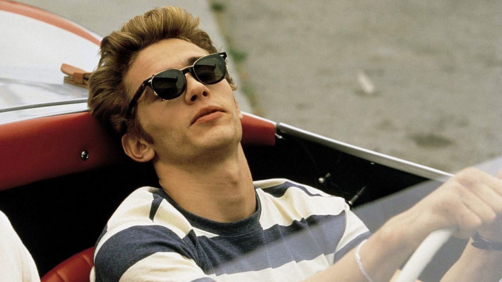James Franco w pasiastym T-shircie i ciemnych okularach przeciwsłonecznych, prowadzący kabriolet
