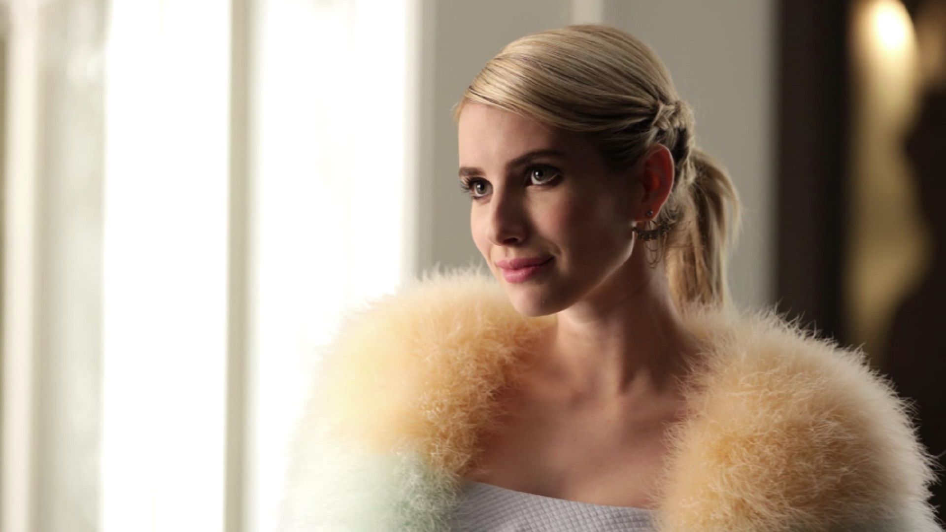 Emma Roberts w futrzanej pelerynie patrzy słodko w lewo