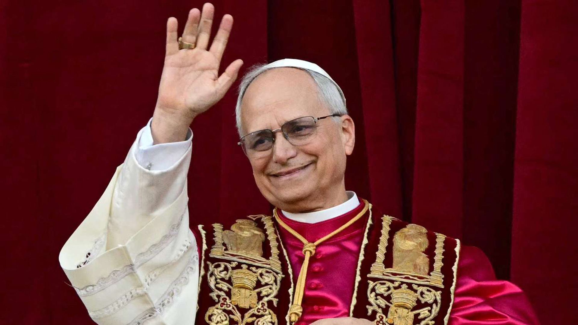 Papież Leon XIV (Robert Francis Prevost), ubrany na czerwono, macha ręką w geście powitania