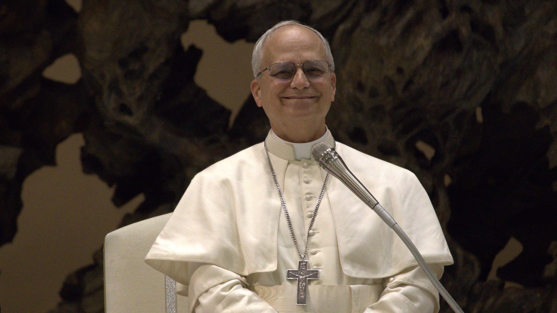 Uśmiechnięty Papież Leon XIV w białych szatach na ciemnym tle