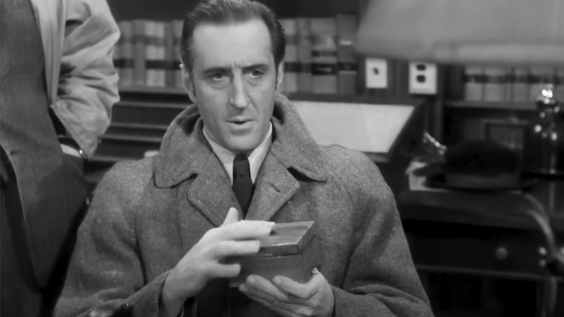 Aktor Basil Rathbone jako Sherlock Holmes trzyma pudełko w rękach i patrzy w dół
