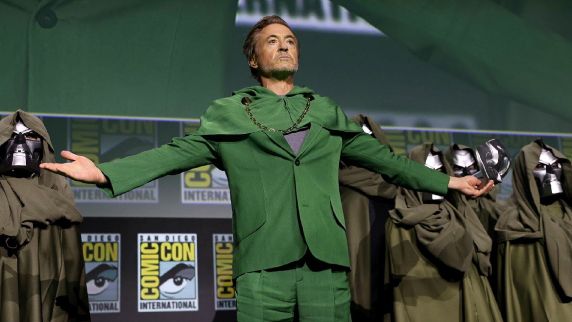 Robert Downey Jr. w zielonym garniturze stoi na scenie, z rozłożonymi ramionami