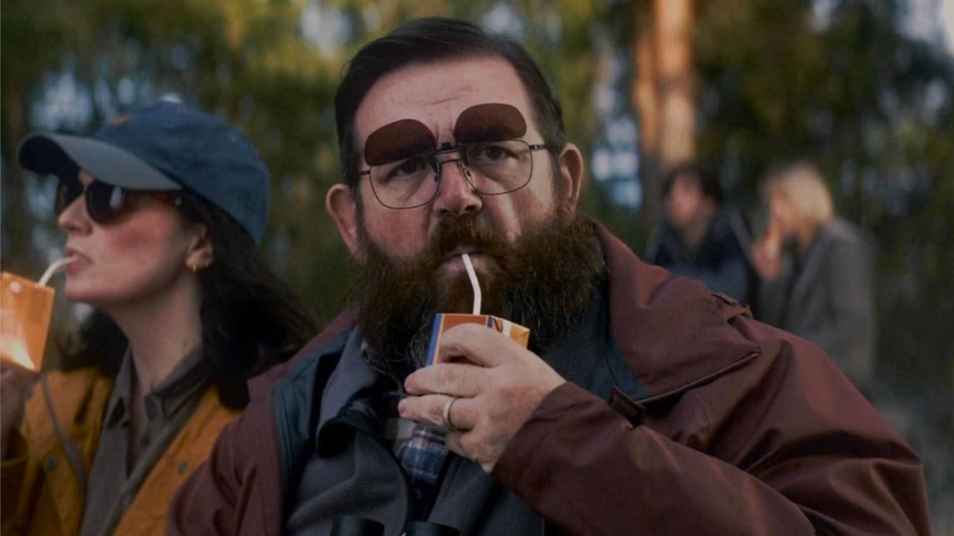 Aktor Nick Frost w okularach, pijący sok z kartonowego pudełka przez słomkę, patrzy w kamerę