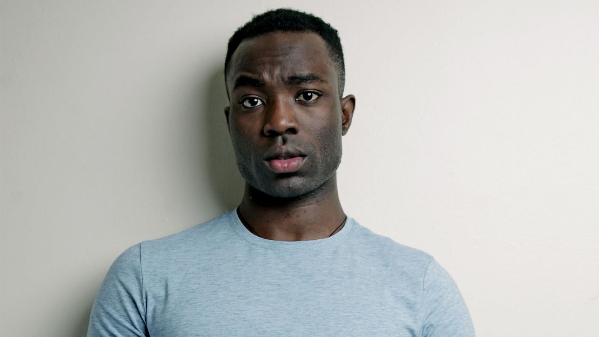 Aktor Paapa Essiedu stoi w niebieskim ubraniu i patrzy w kamerę, unosząc brew