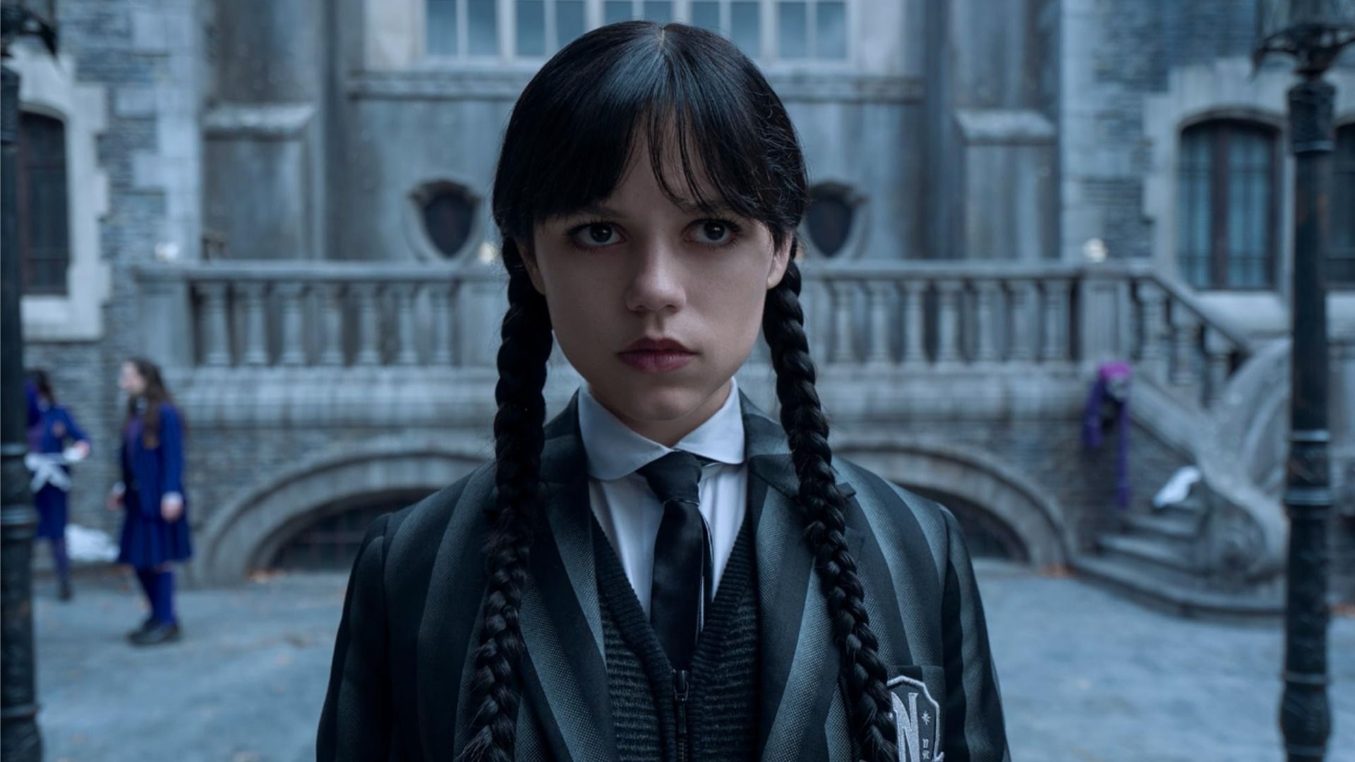 Aktorka Jenna Ortega w szkolnym stroju w scenie z serialu 'Wednesday', patrzy bez emocji na bok