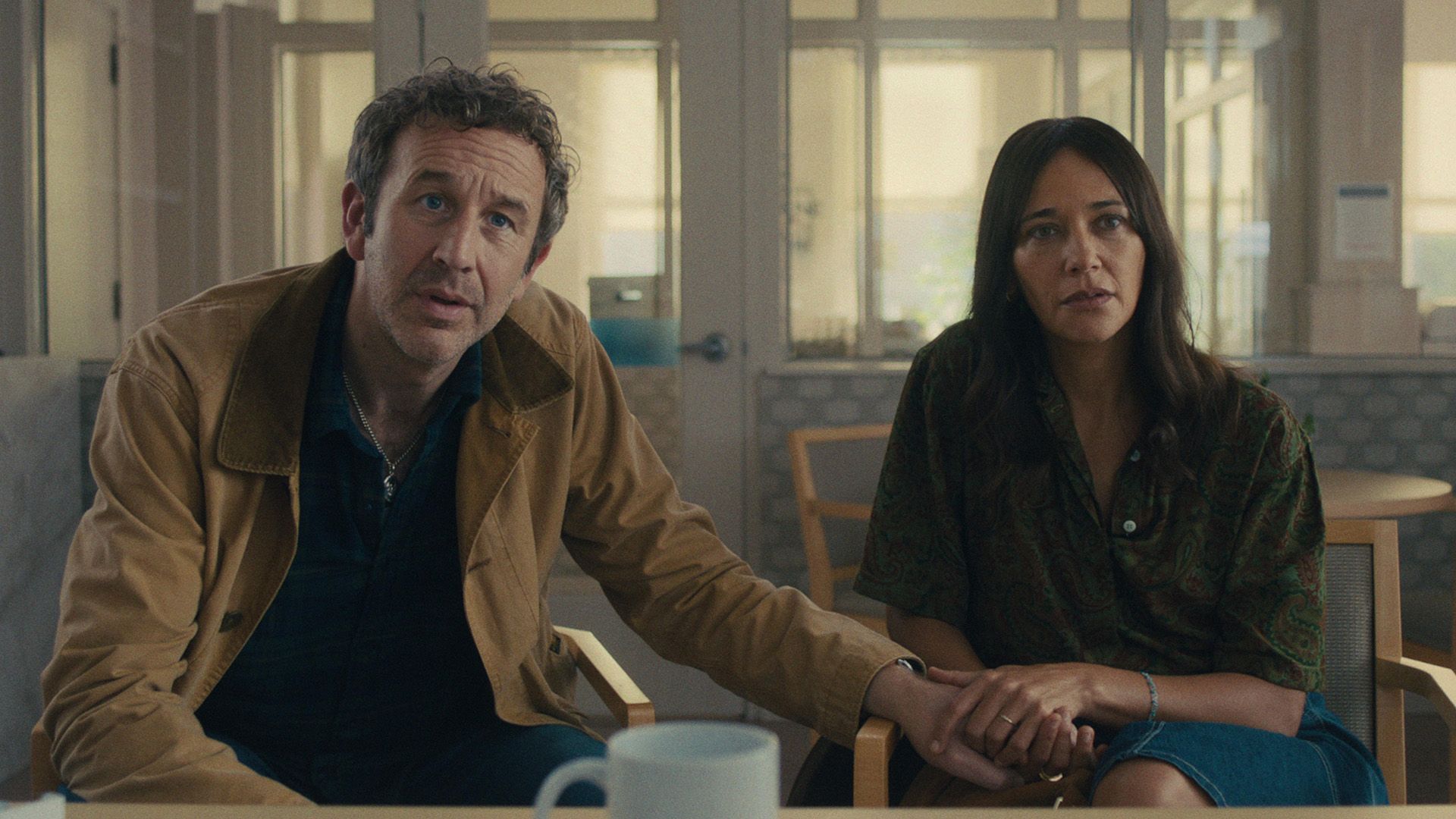 Chris O'Dowd i Rashida Jones siedzą na krzesłach z zaniepokojonymi wyrazami twarzy, trzymając się za ręce