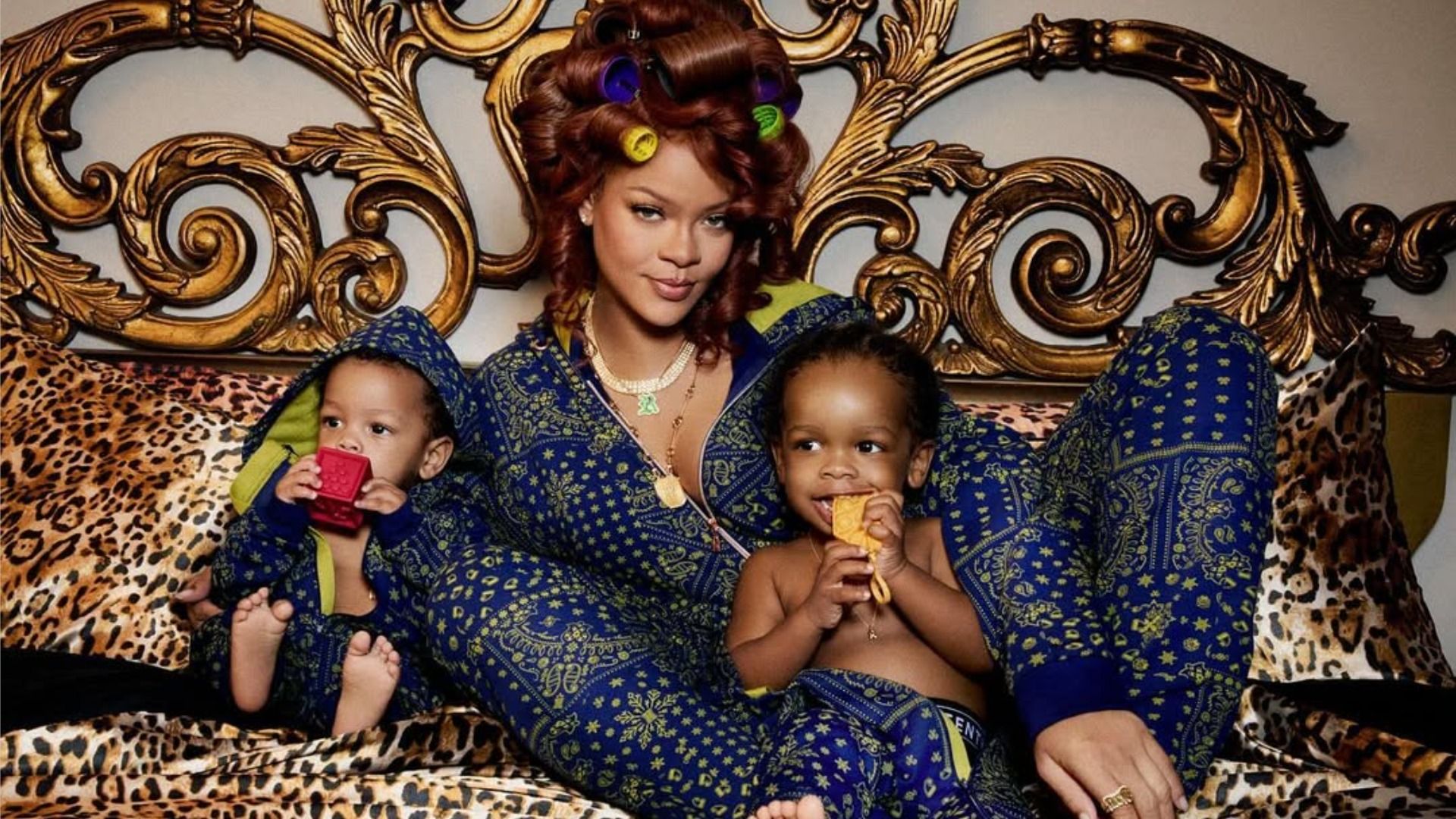Piosenkarka Rihanna leży na łóżku ze swoimi synami RZA i Riot, patrząc na kamerę z uśmiechem