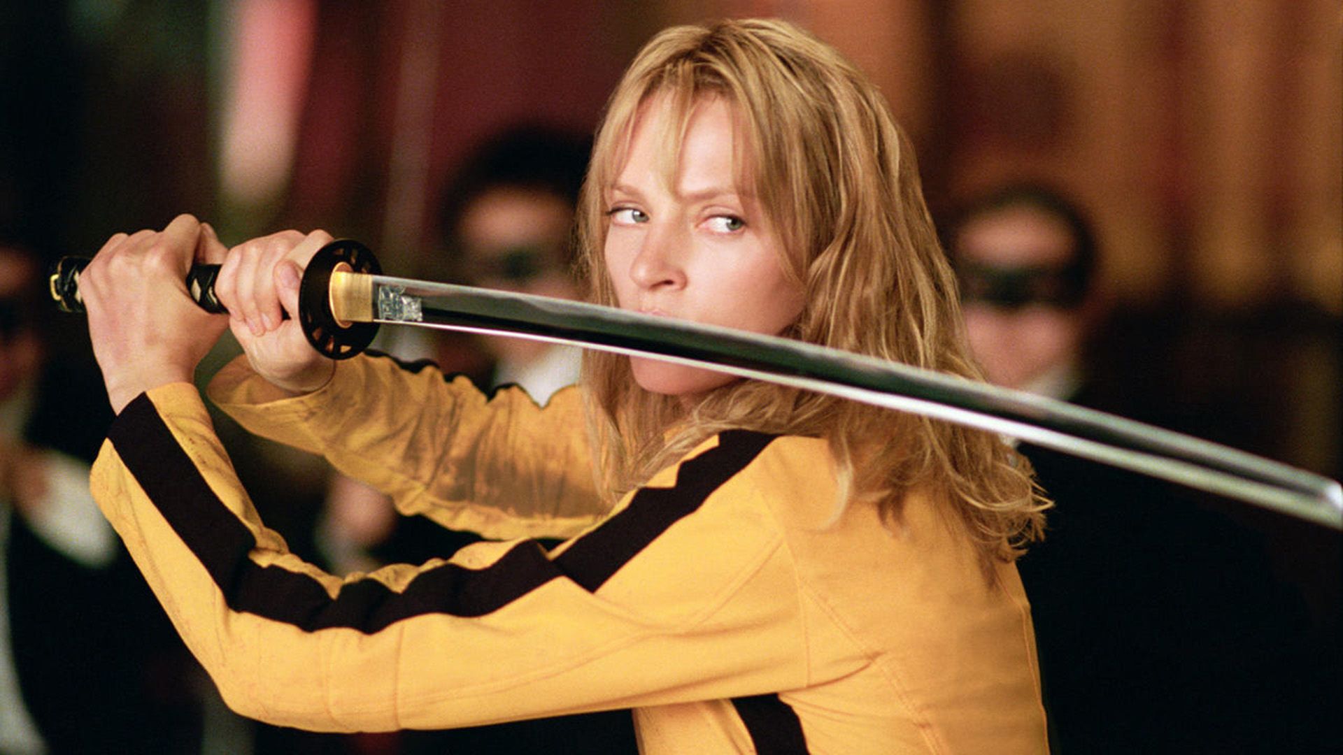 Uma Thurman w żółtym swetrze z czarnymi paskami trzyma katanę przed twarzą w 'Kill Bill'