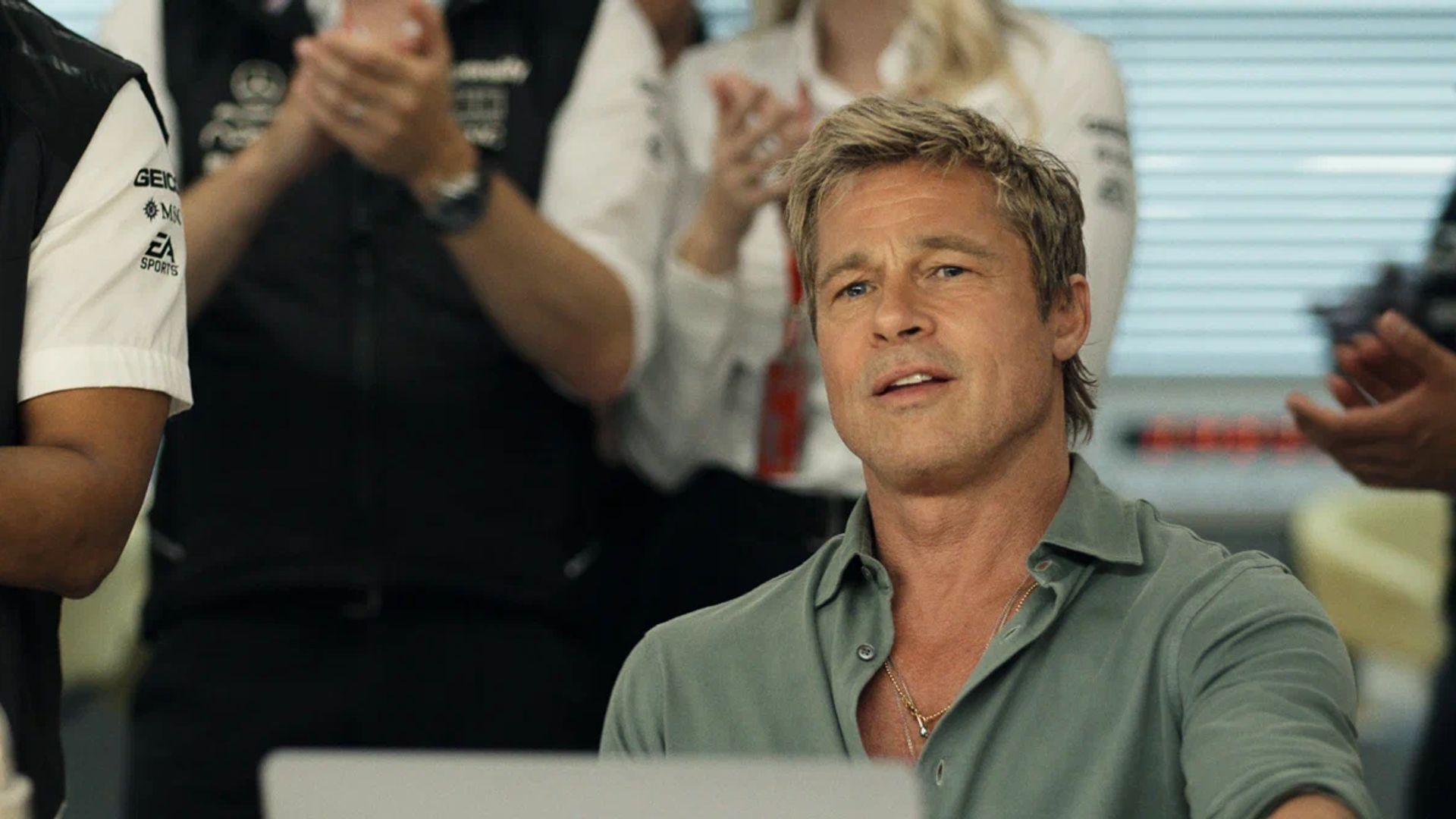 Brad Pitt w rozpiętej koszuli siedzi przed laptopem z oklaskującymi ludźmi w tle