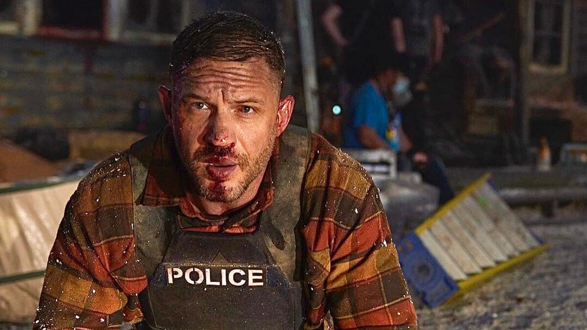 Tom Hardy w kamizelce kuloodpornej z posiniaczoną twarzą klęczy na miejscu zdarzenia