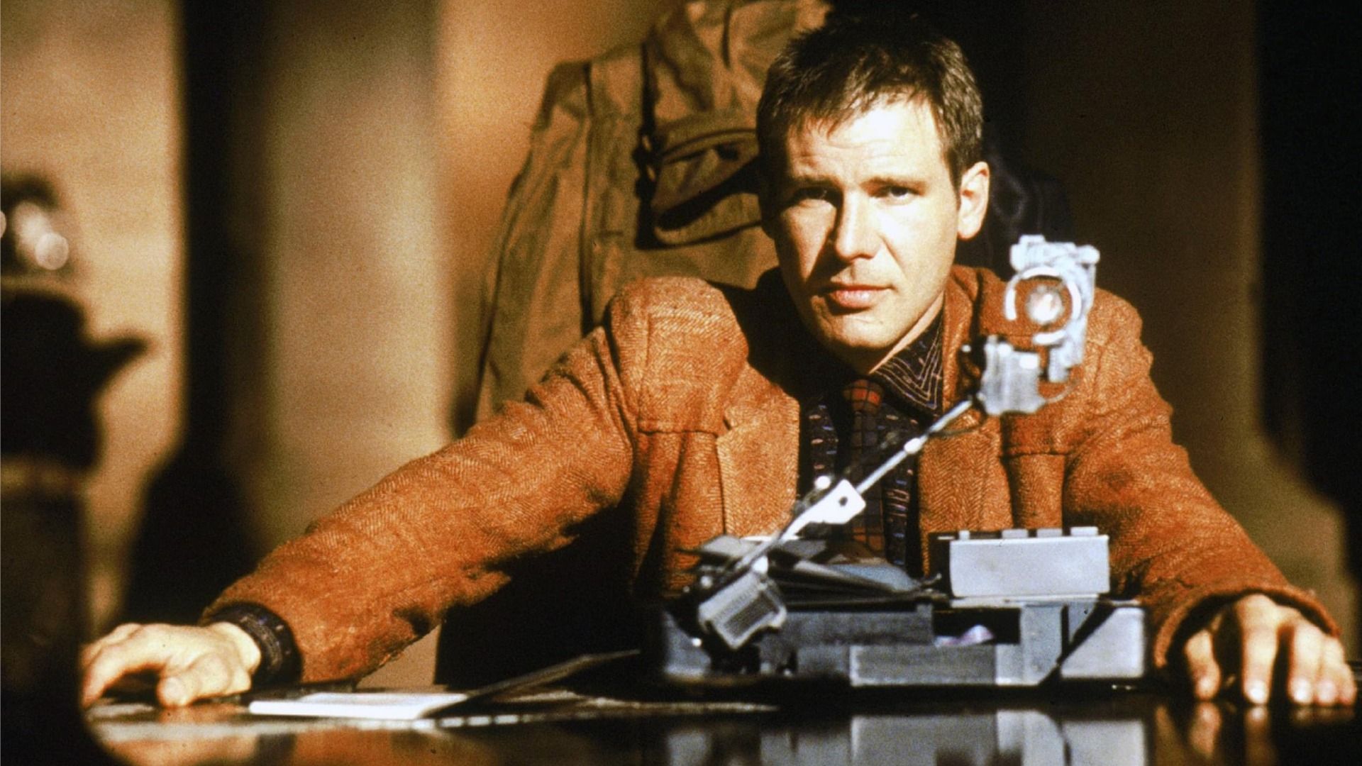 Aktor Harrison Ford jako Rick Deckard siedzi przy stole w brązowej kurtce
