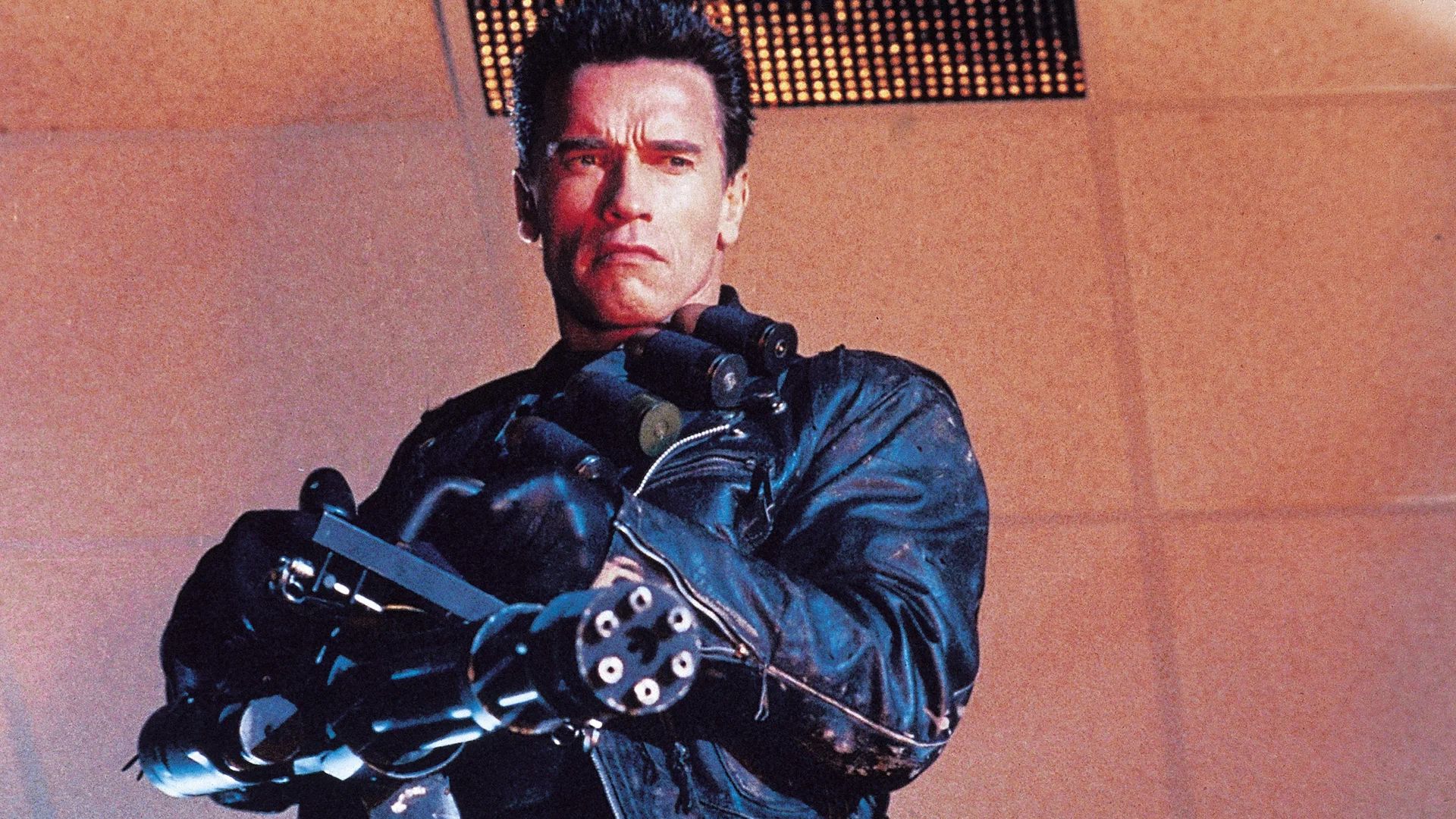 Arnold Schwarzenegger w czarnej skórzanej kurtce trzymający minigun