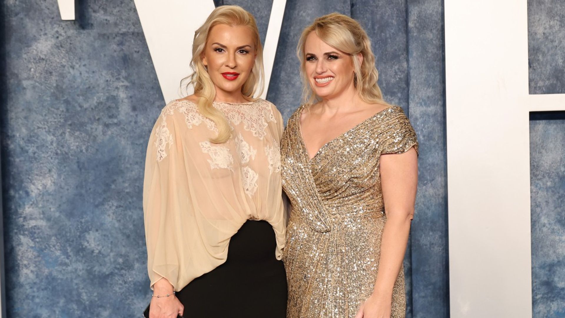 Rebel Wilson i Ramona Agruma stoją w sukienkach na jasnym tle