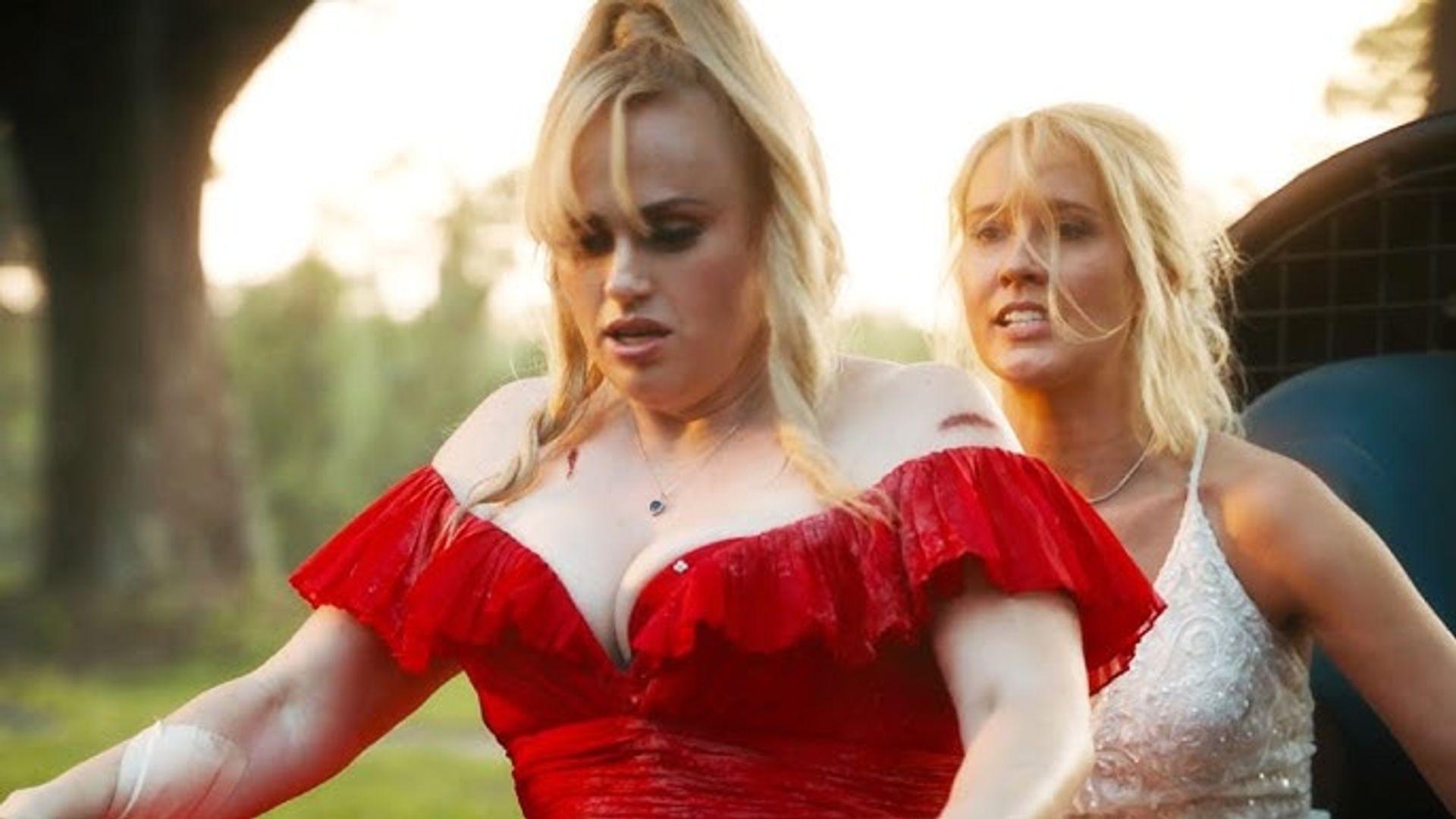 Rebel Wilson w czerwonej sukience i Anna Camp w białej jadące na rowerach