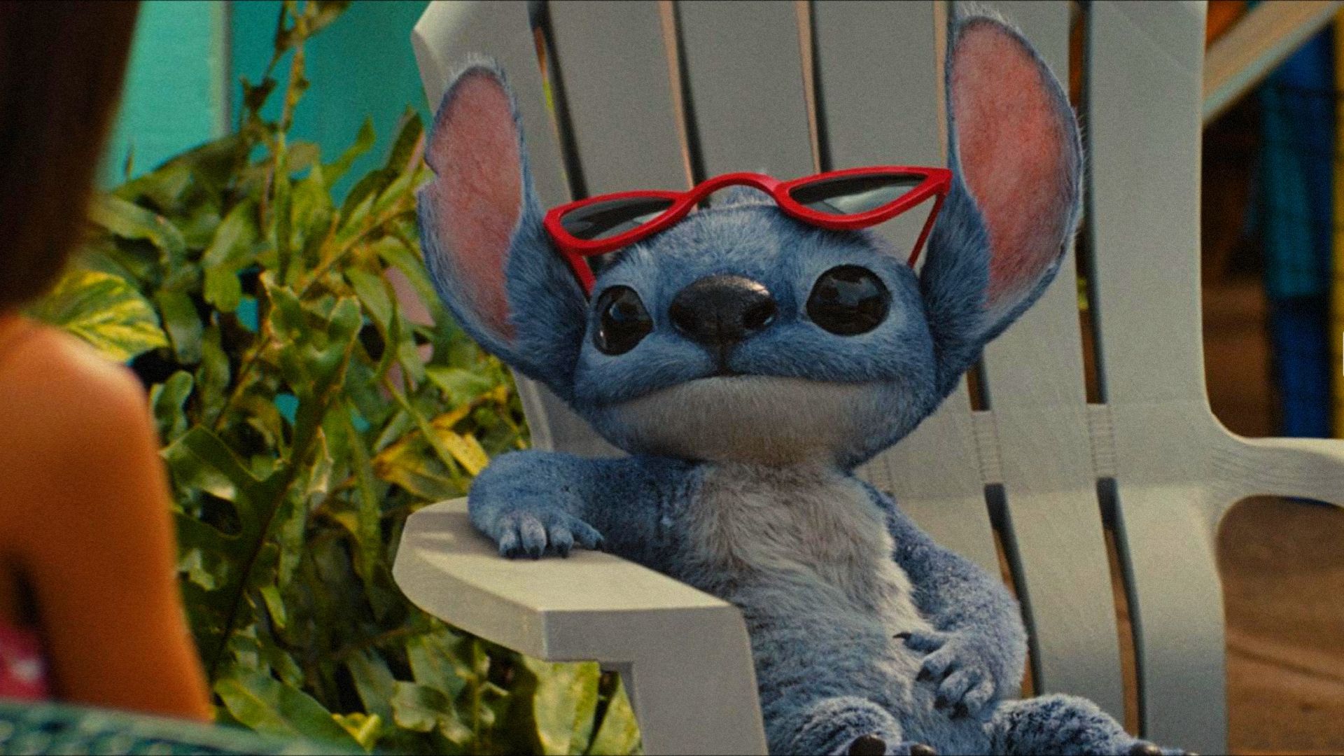 Niebieski kosmita Stitch siedzi na leżaku w okularach i patrzy w bok