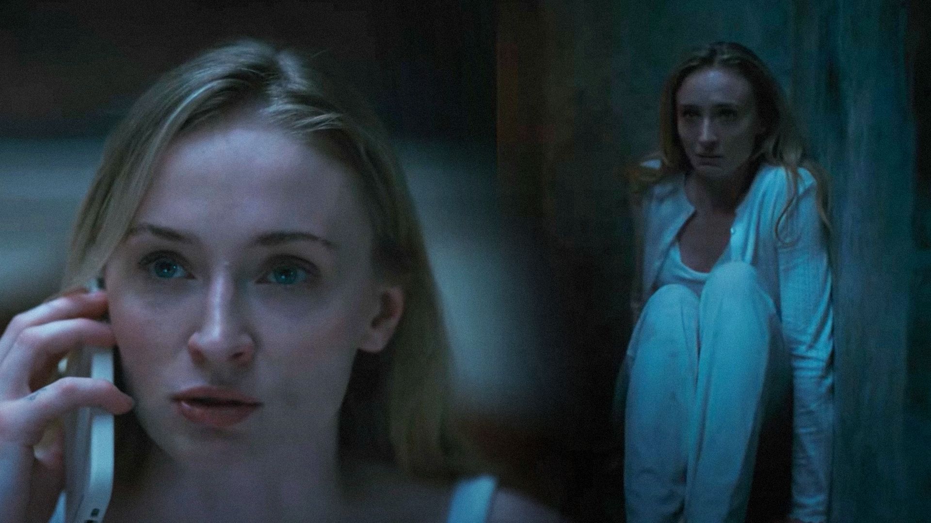 Actress Sophie Turner with a phone in her hand sitting against the wall in a nightgown