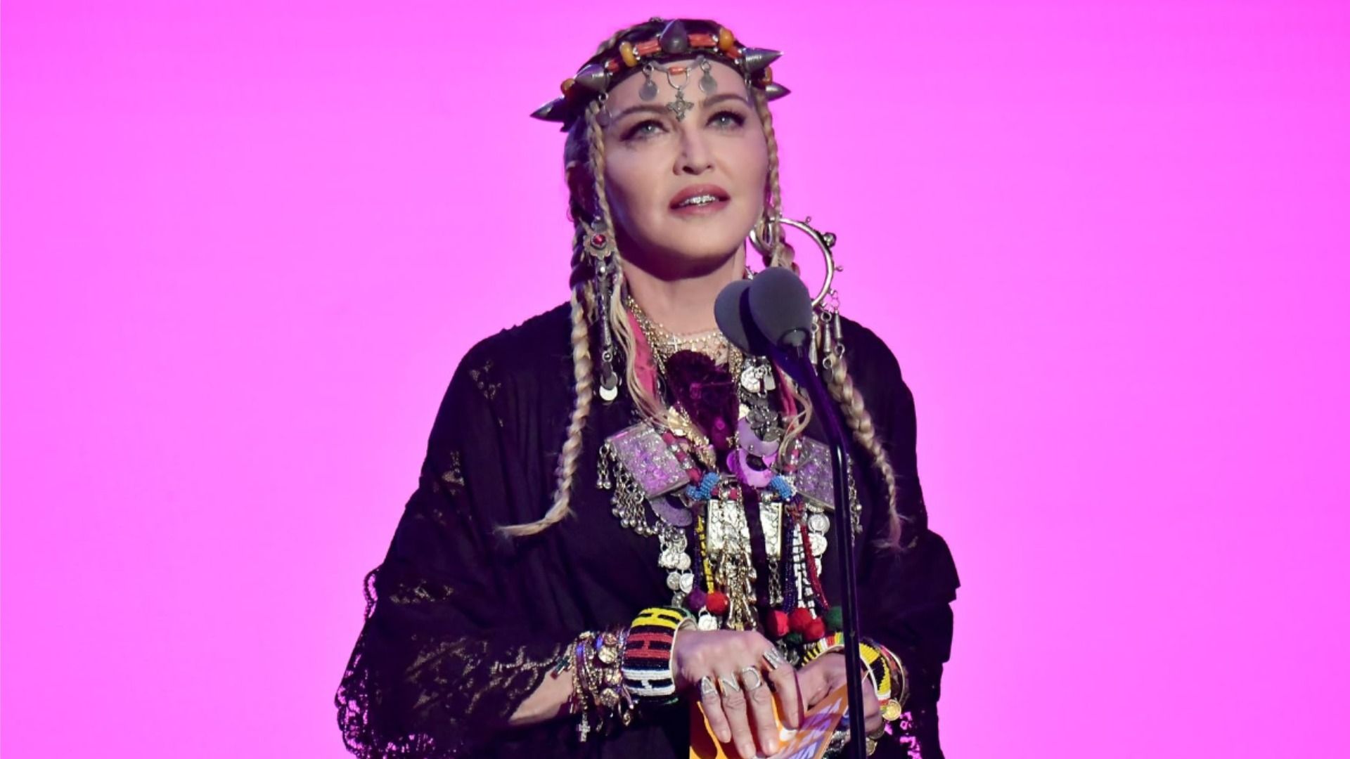 Piosenkarka Madonna w czarnej sukience na różowym tle patrzy w górę