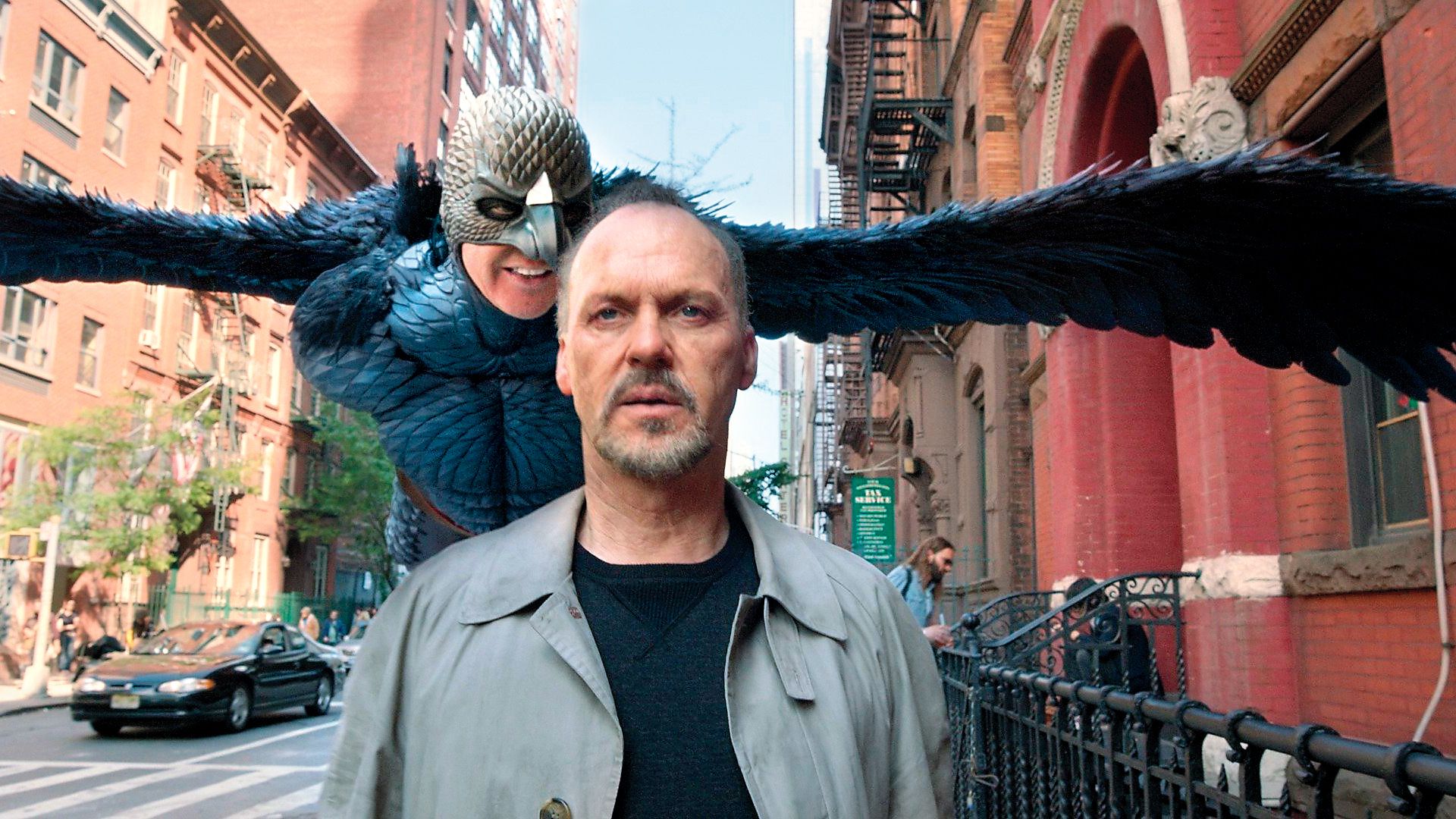 Michael Keaton idzie ulicą, podczas gdy za nim unosi się fantastyczna postać ze skrzydłami i ptasią maską